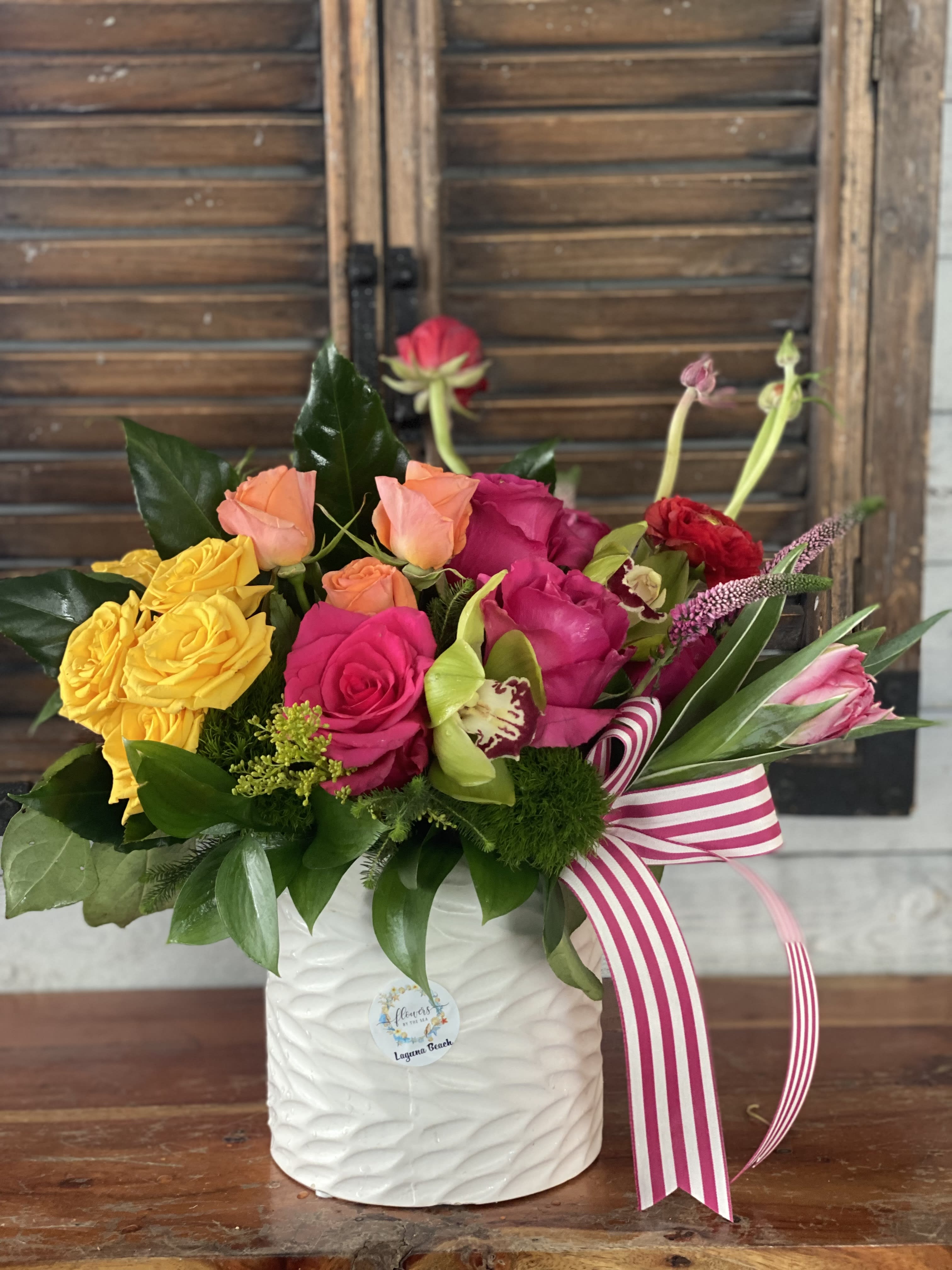 Colorful rose arrangement in a white ceramic vase with a striped ribbon