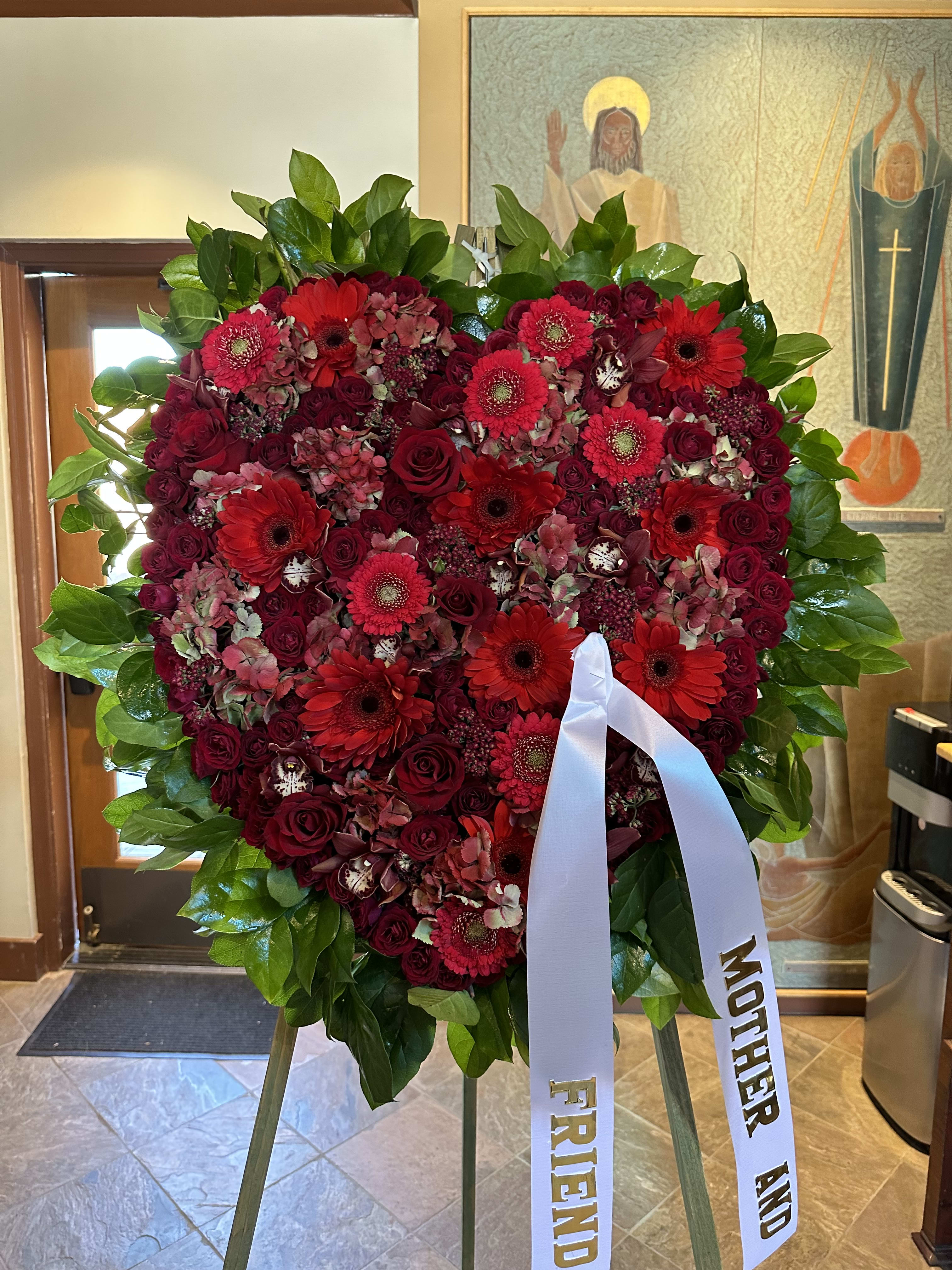 Heart-shaped red floral wreath on an easel with white ribbons