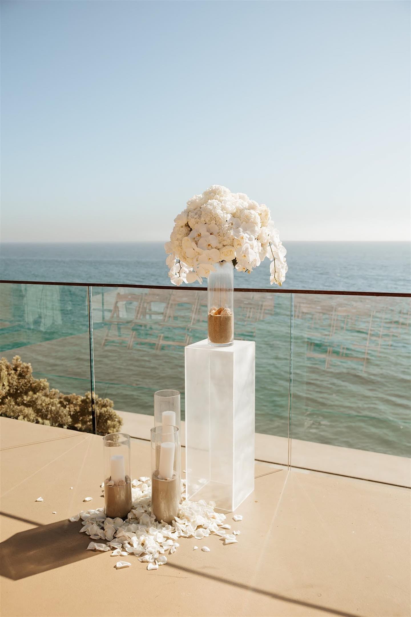 White orchid arrangement on a tall clear pedestal by the ocean