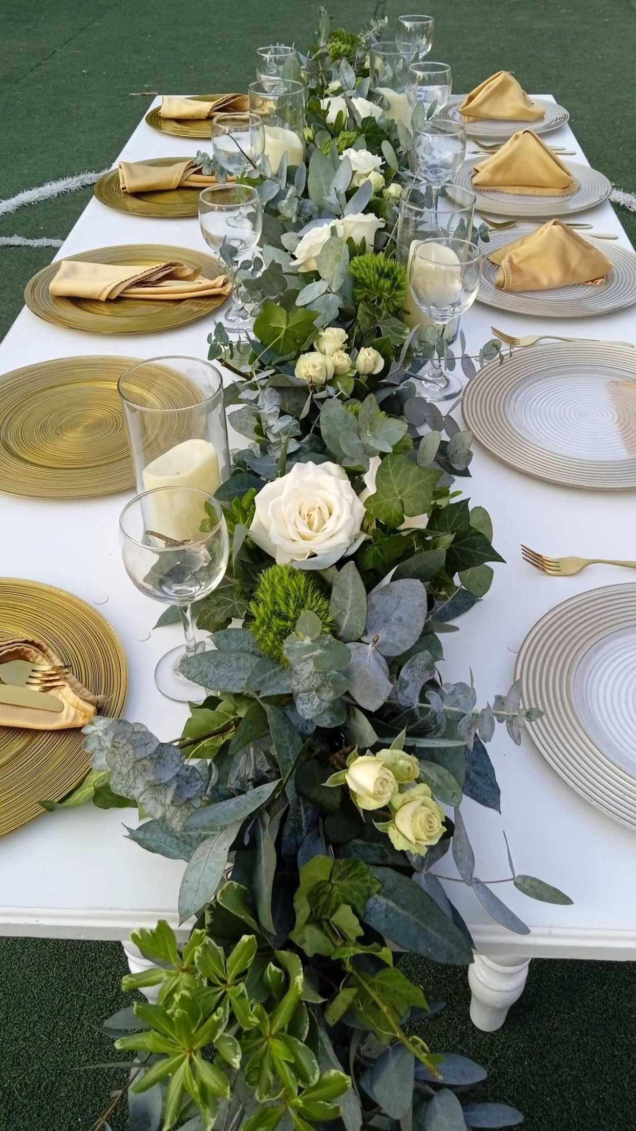 Long table centerpiece with white roses and greenery on a set dining table