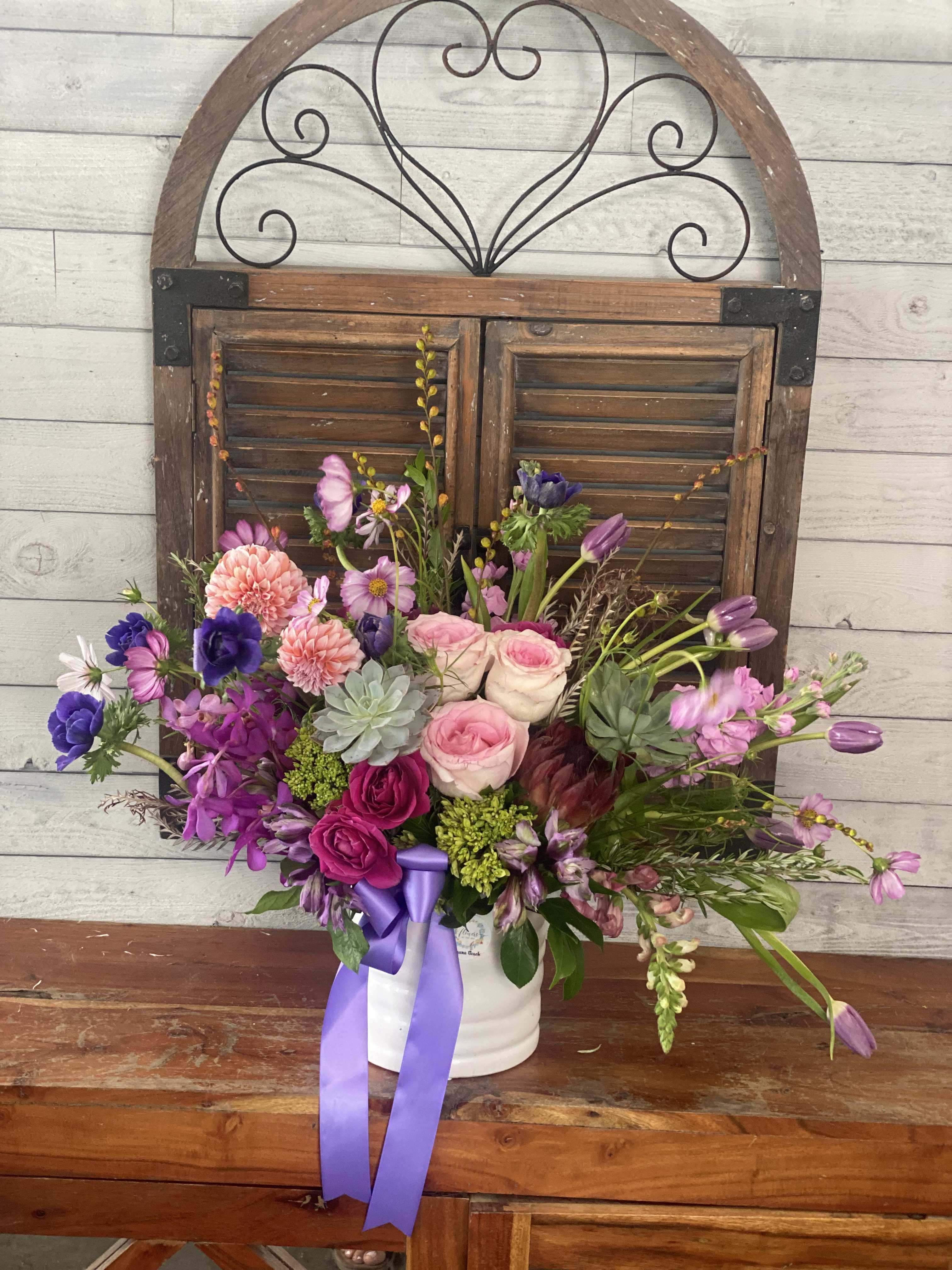 Mixed pink and purple flower arrangement in a white container with a ribbon