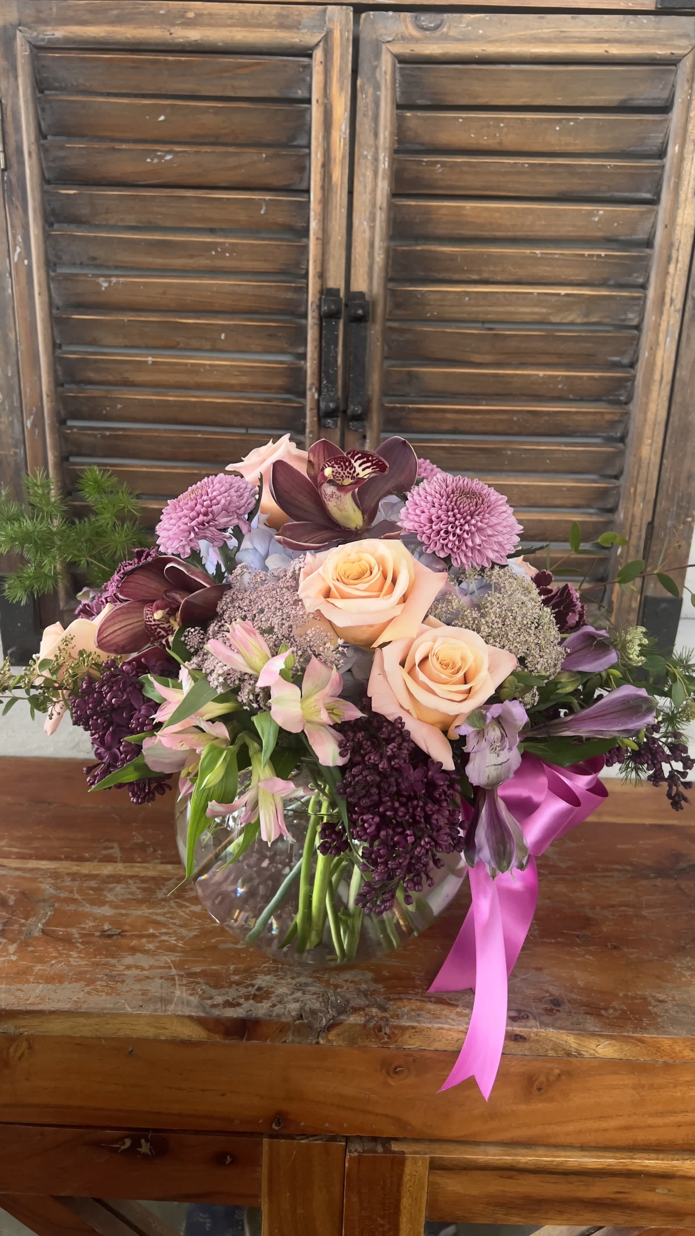 Mixed bouquet of peach roses, orchids, and purple blooms in a glass vase