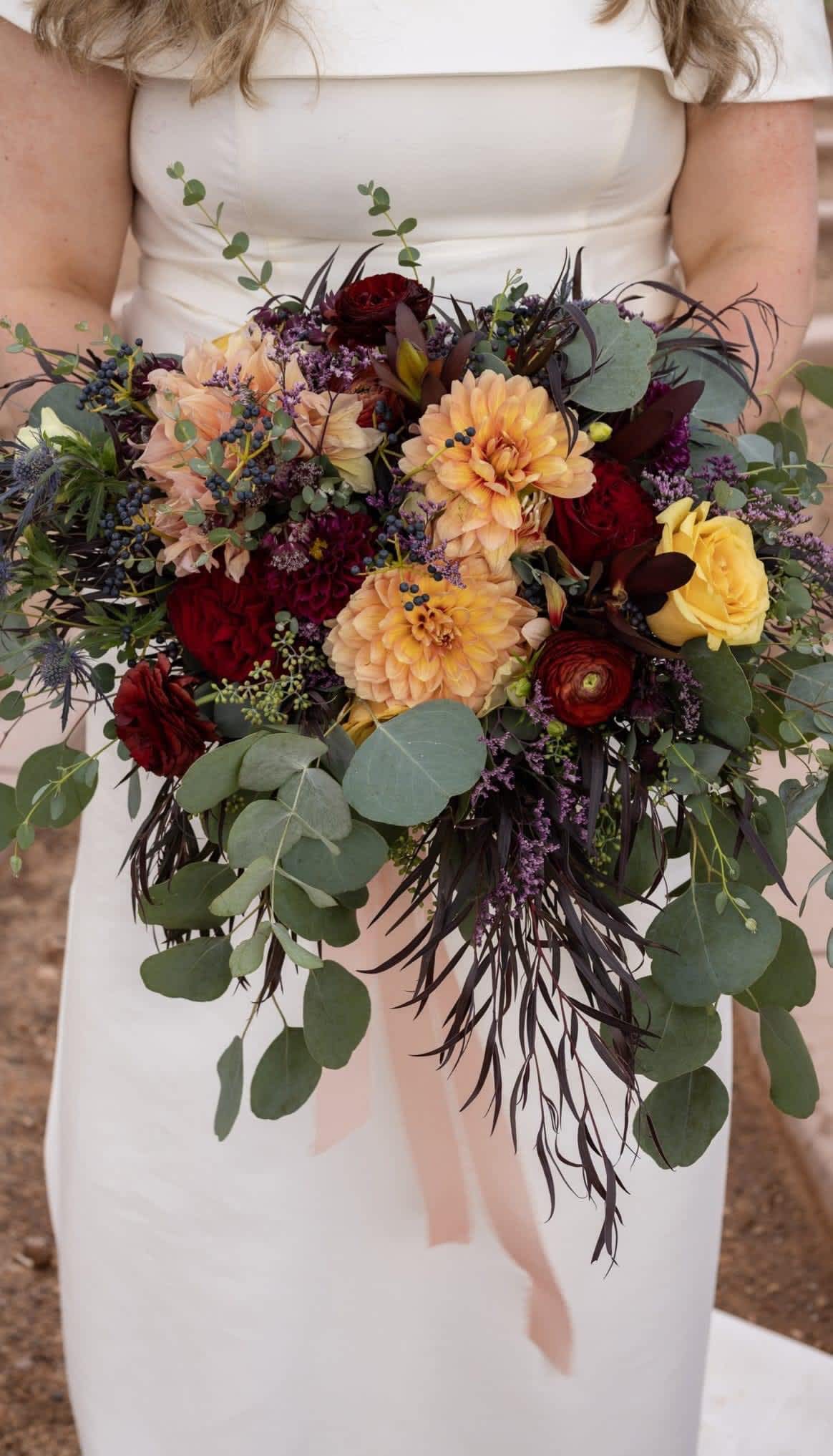 Bride holding a bouquet of peach, red, and yellow flowers with eucalyptus