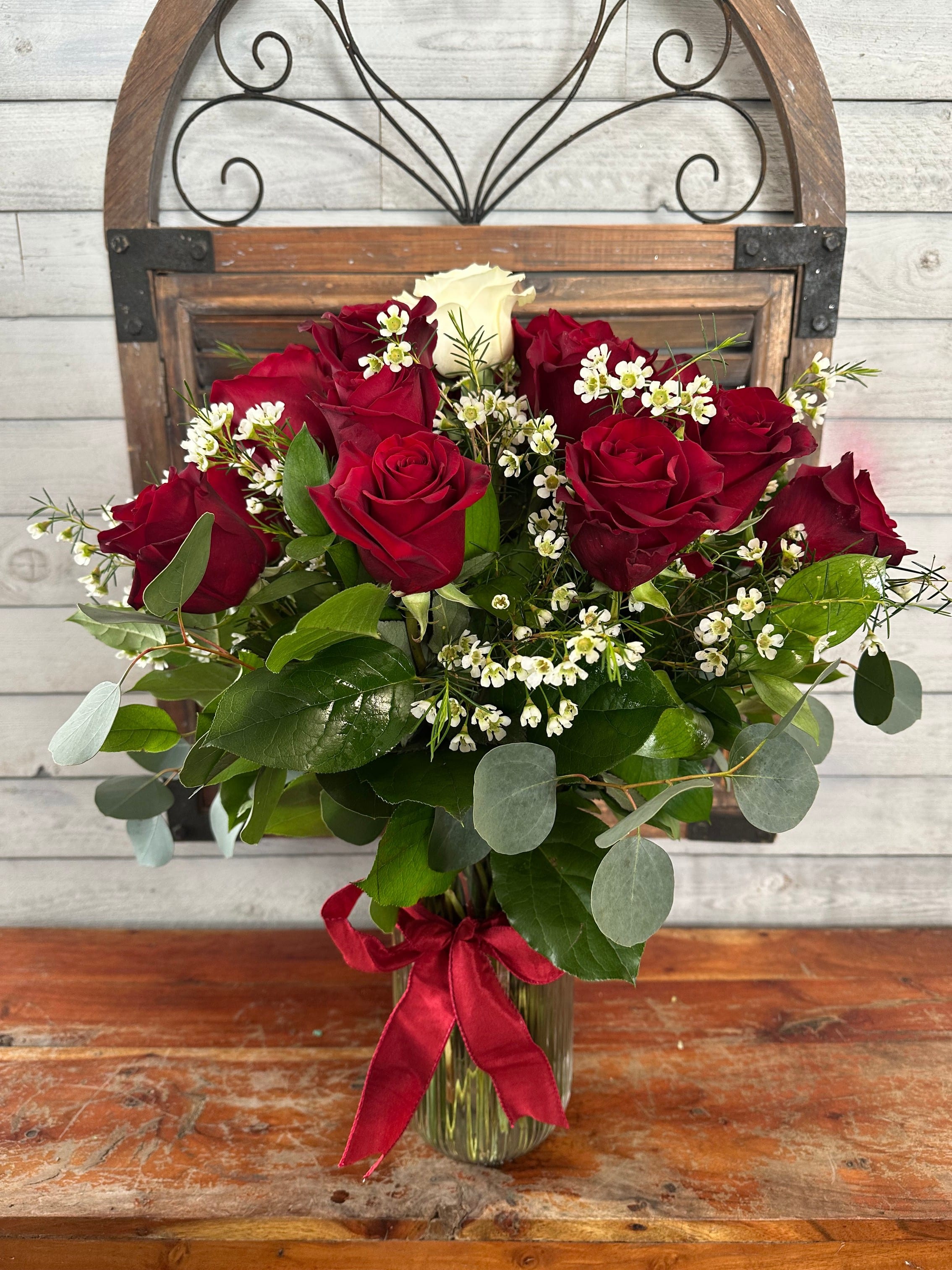 Red roses and white filler flowers in a glass vase with a red ribbon