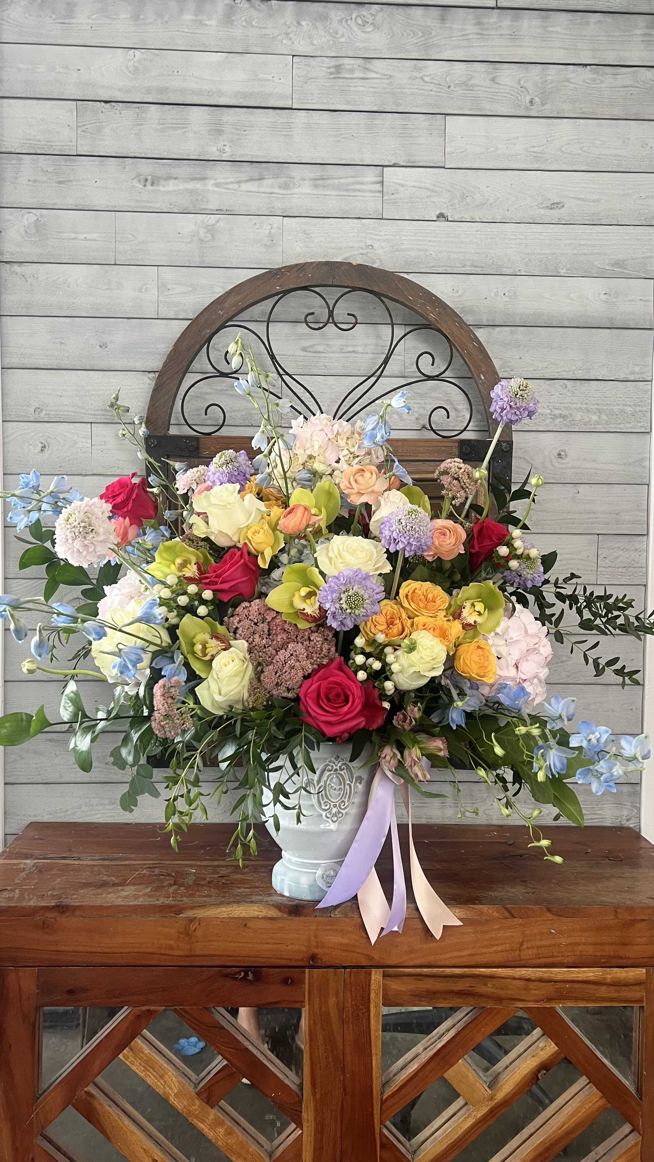 Colorful mixed flower arrangement in a white vase with ribbon tails