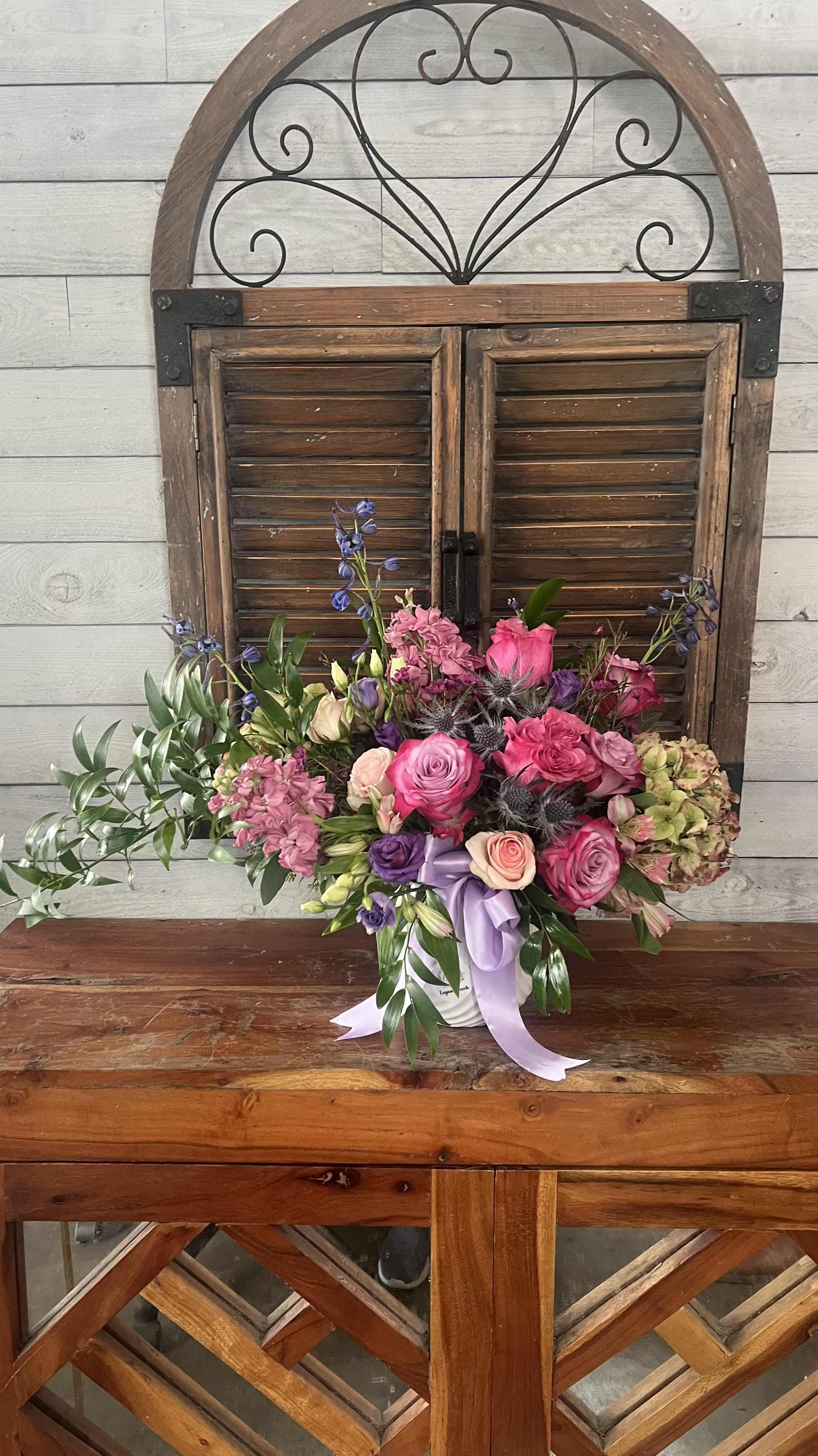 Pink and purple mixed flower arrangement in a white container with ribbon