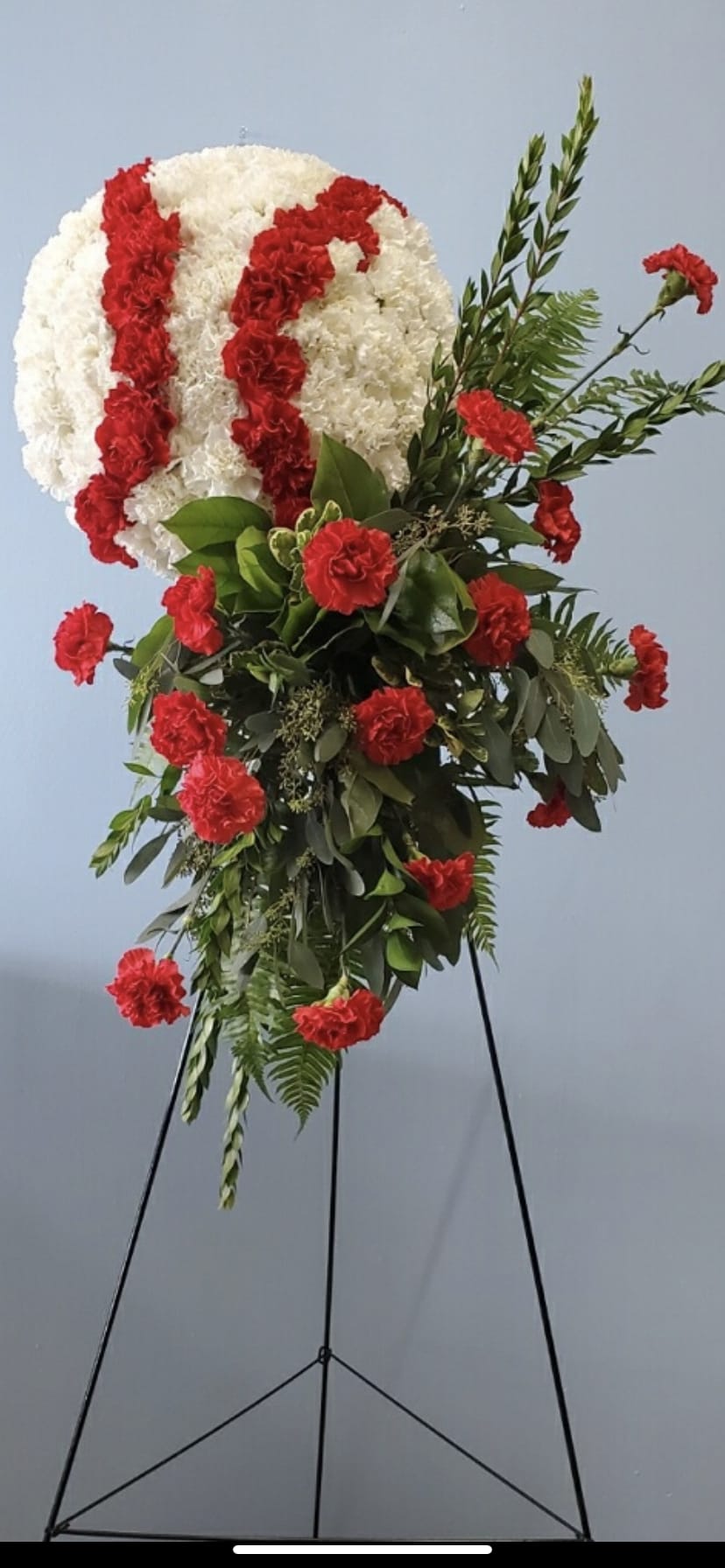 Standing floral spray with white and red carnations on a black easel