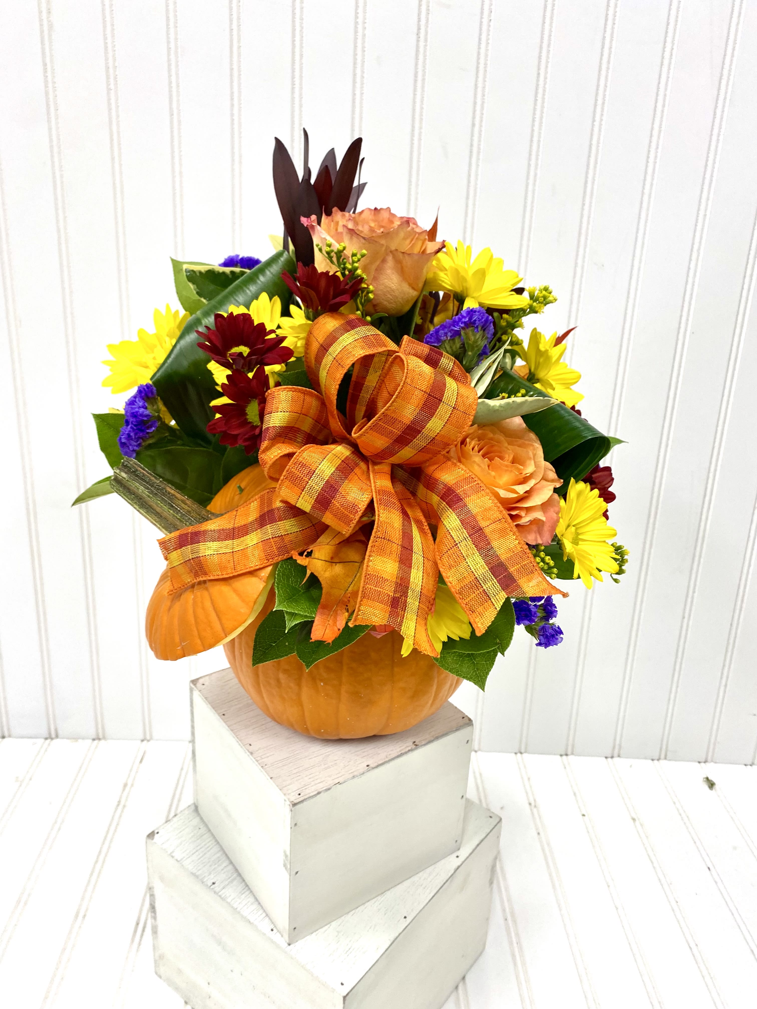 Fall floral arrangement in a pumpkin container with an orange ribbon bow