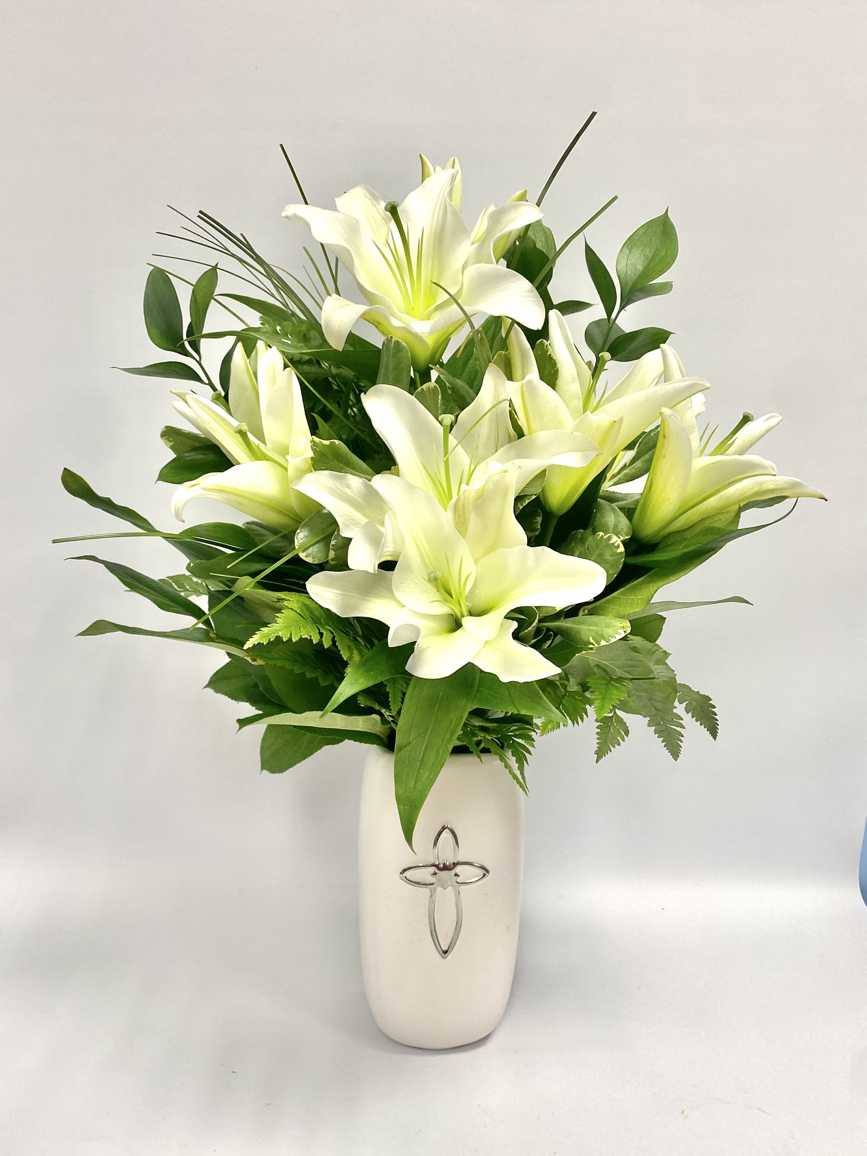 White lilies arranged in a white vase with green foliage