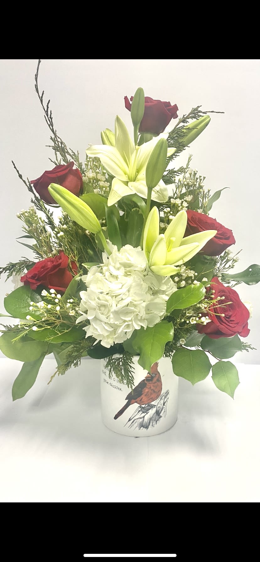 Red roses and white lilies in a white vase with a hydrangea bloom