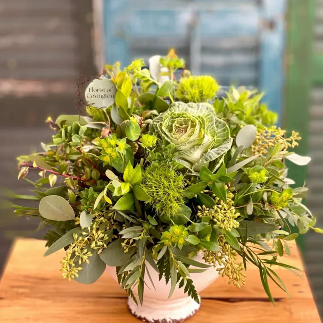 Green floral arrangement in a white vase with cabbage rose and mixed foliage