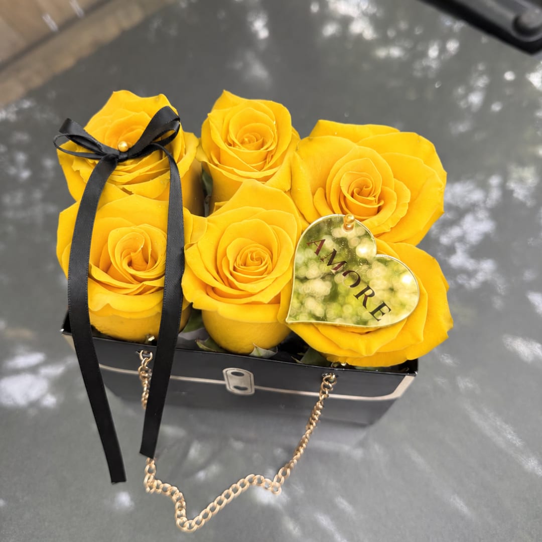 Yellow roses arranged in a small black box with a ribbon and heart tag