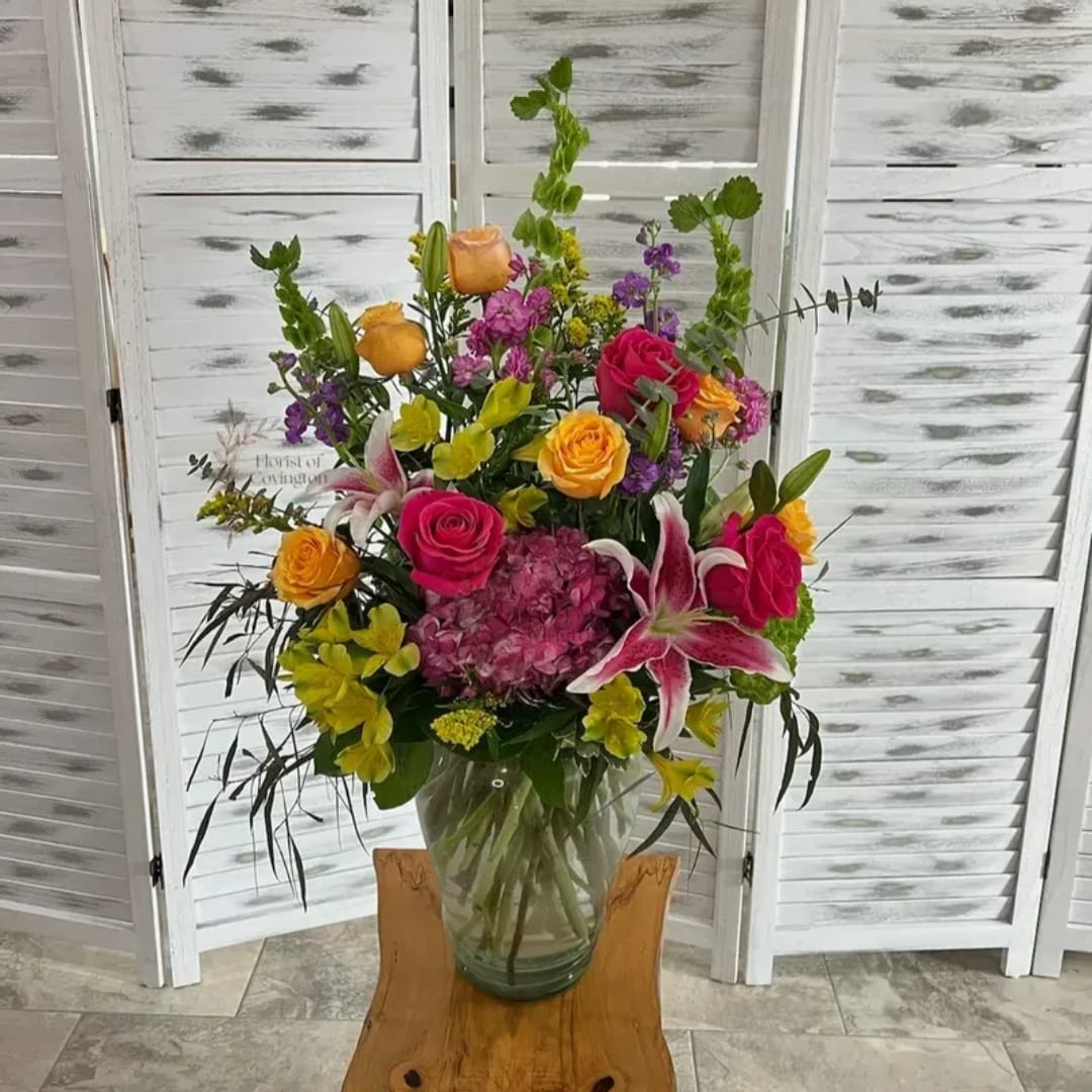 Mixed bouquet of roses, lilies, and purple blooms in a glass vase