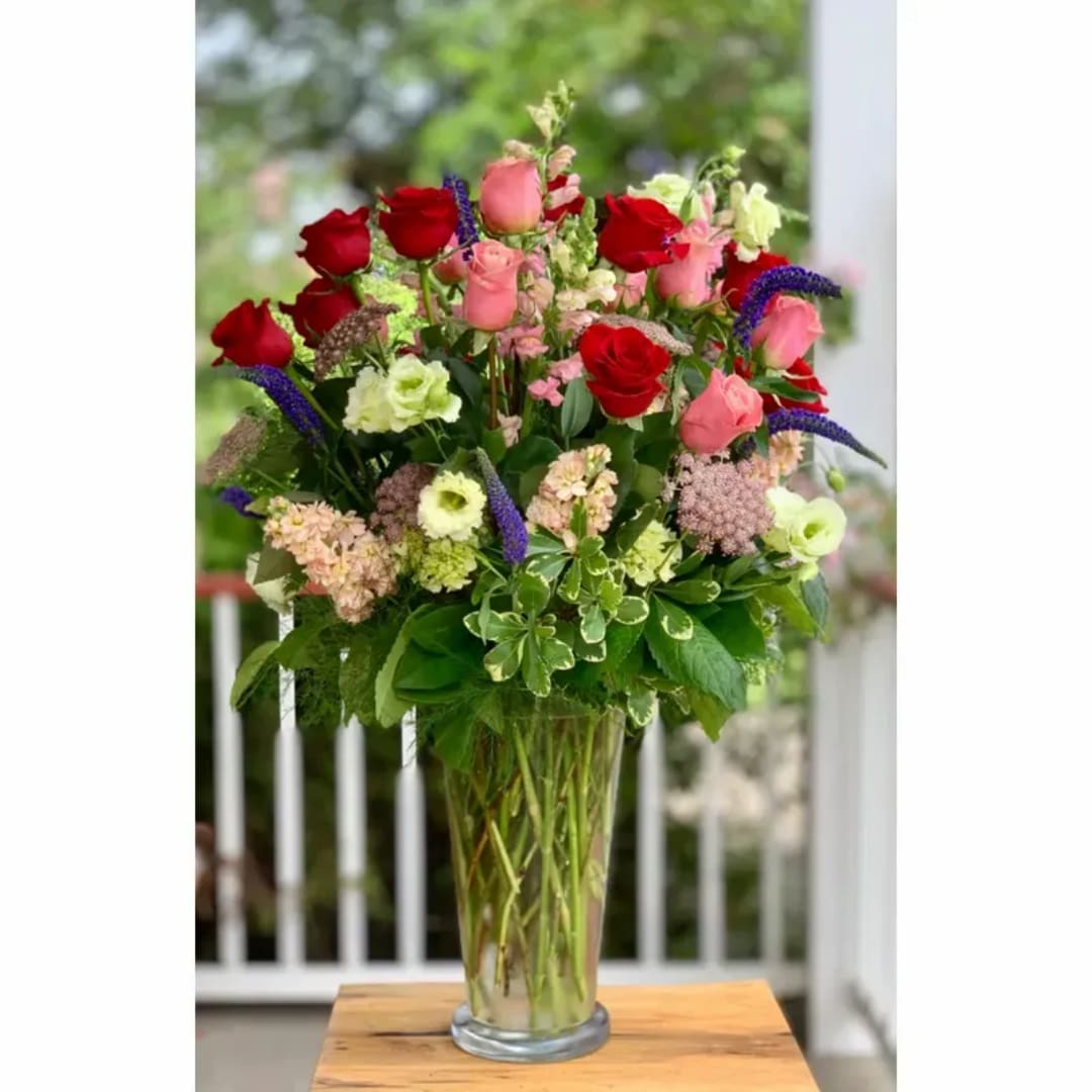 Tall mixed bouquet of red and pink roses in a clear glass vase