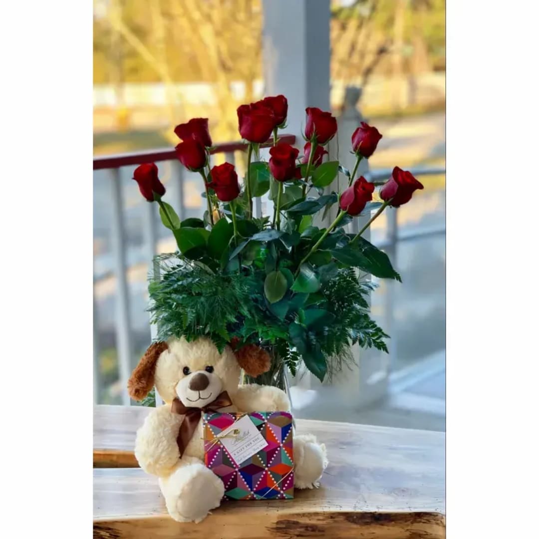 Red roses in a vase with a teddy bear and gift box