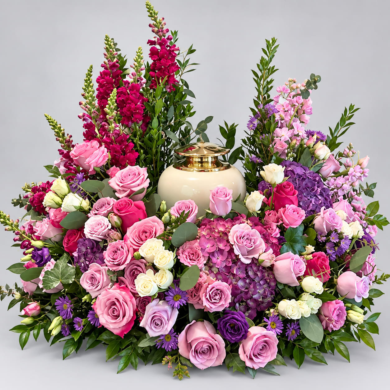 Large floral arrangement of pink, purple, and white roses around a cream urn