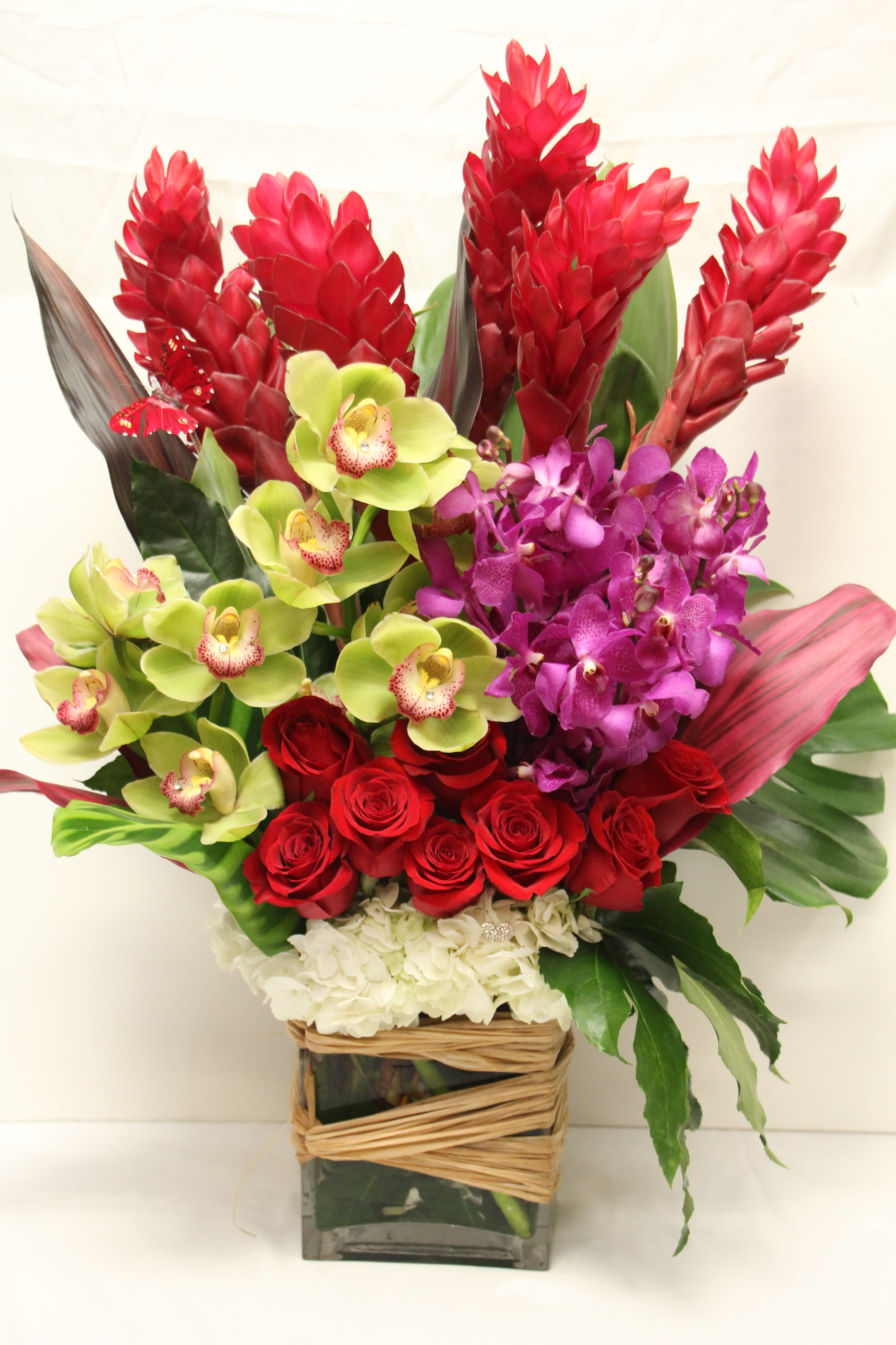 Red roses and orchids arranged in a square glass vase