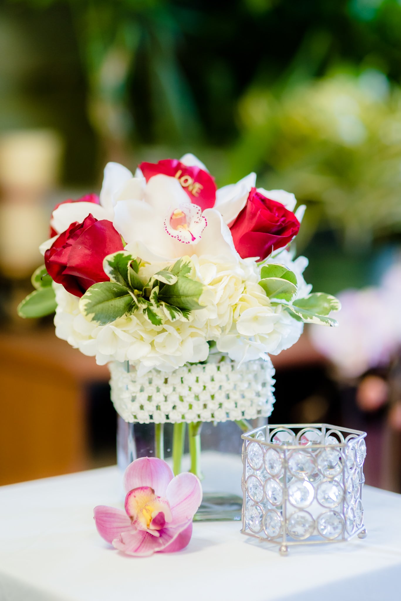 White hydrangea and red roses in a clear vase with a pink orchid bloom