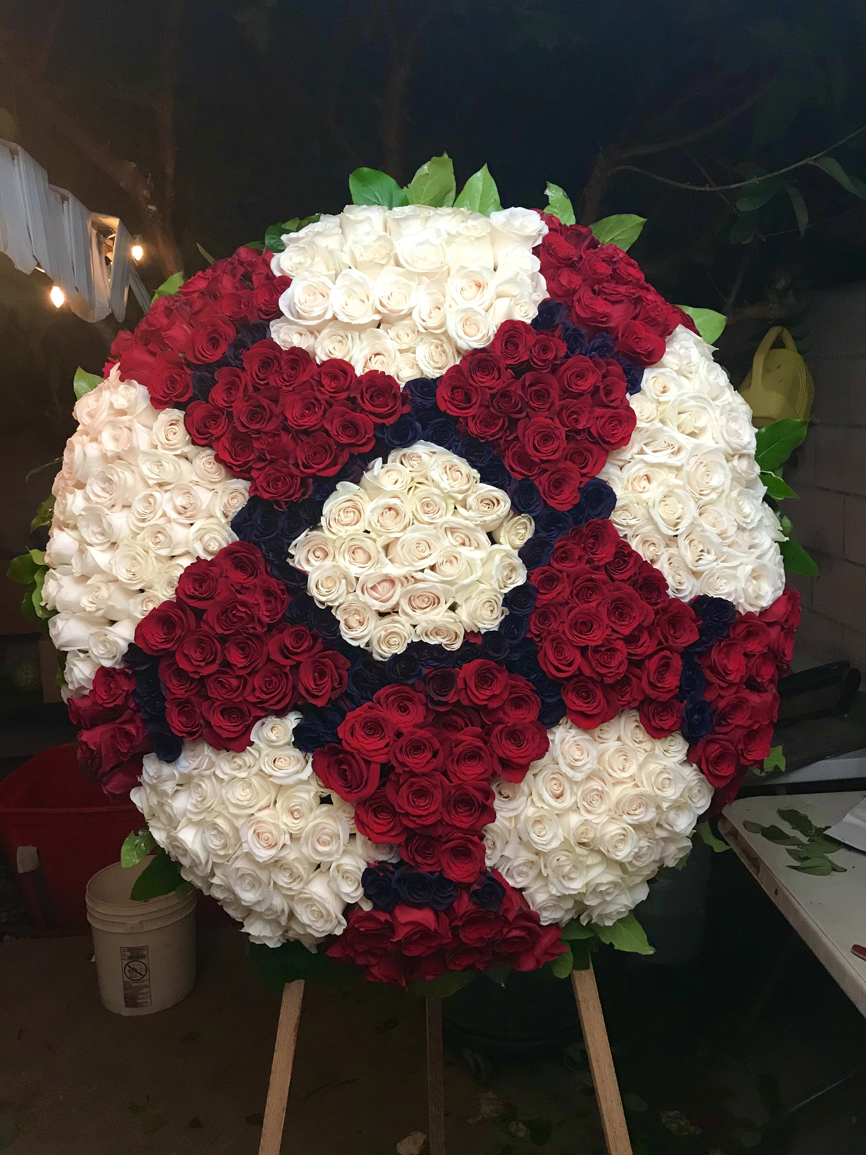 Large circular arrangement of red, white, and dark blue roses on an easel