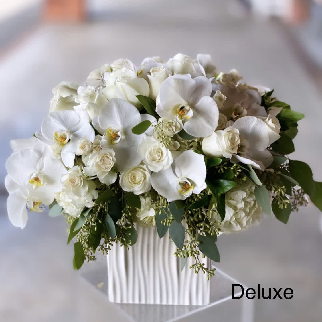 White orchids and roses arranged in a ribbed white vase