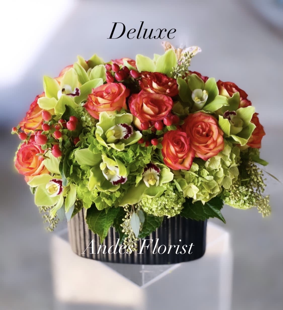 Bouquet of orange roses and green orchids in a black vase