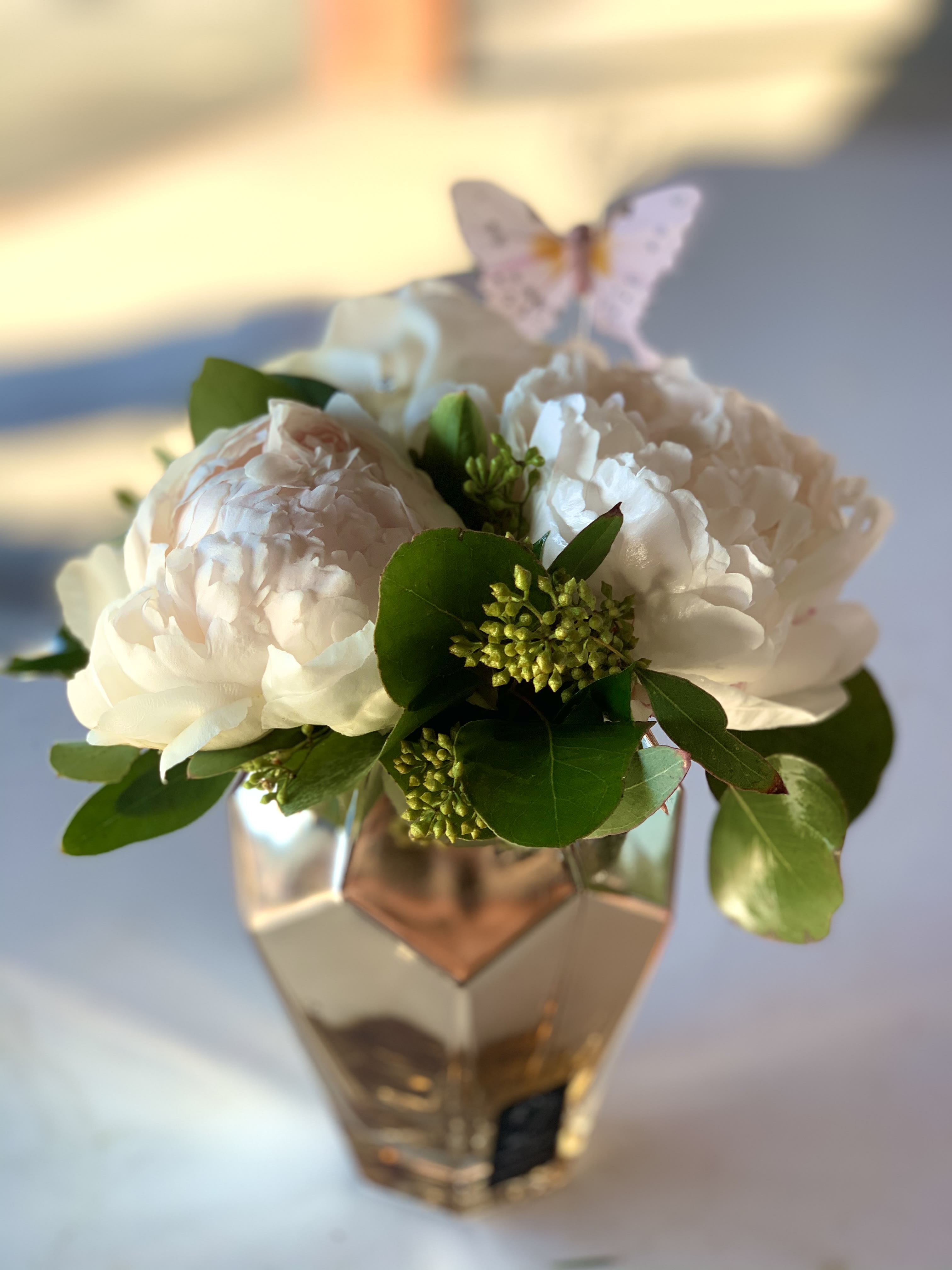 White peonies in a faceted glass vase with a butterfly pick