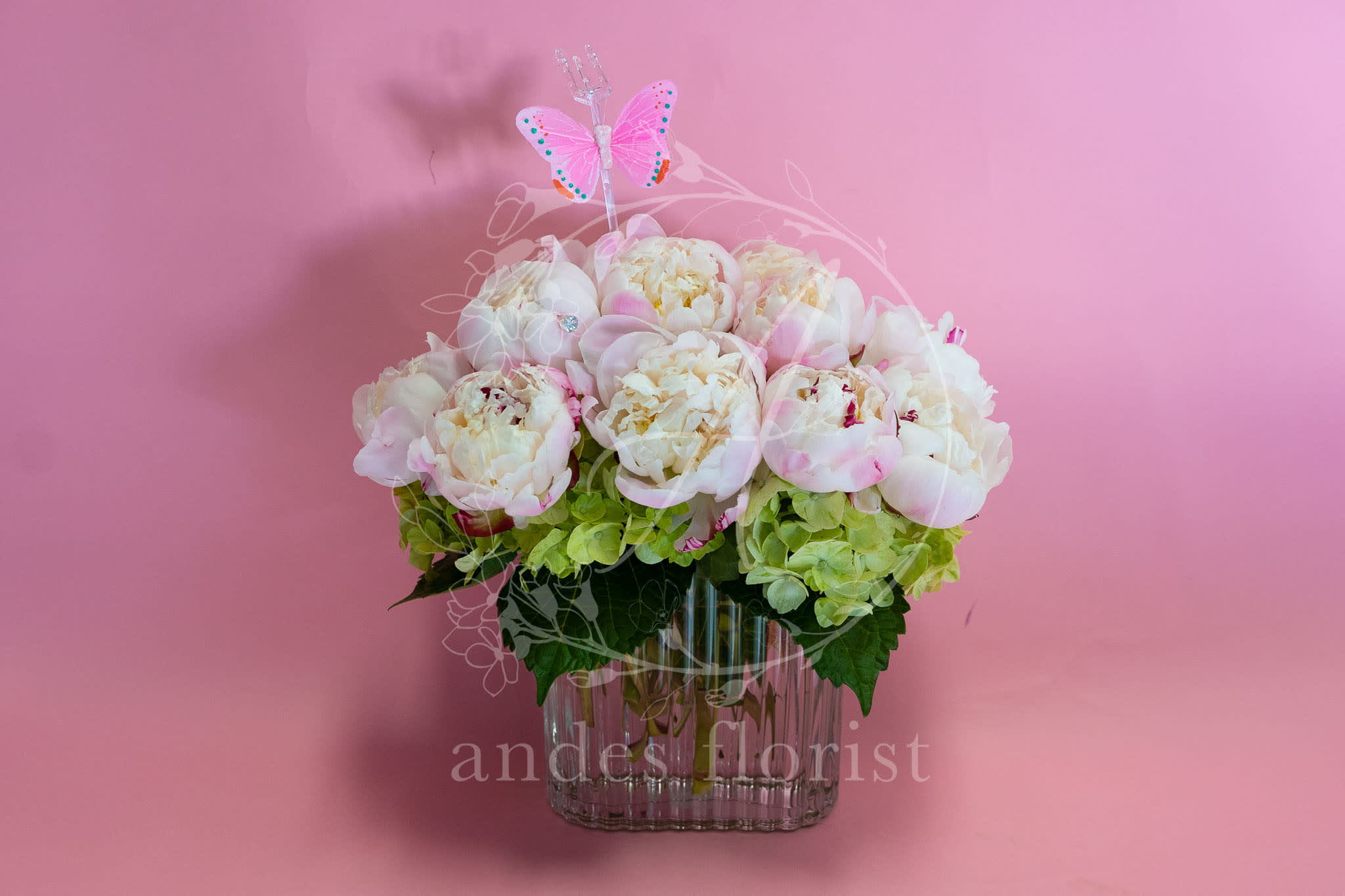 Pink and white peonies in a clear glass vase with a butterfly pick