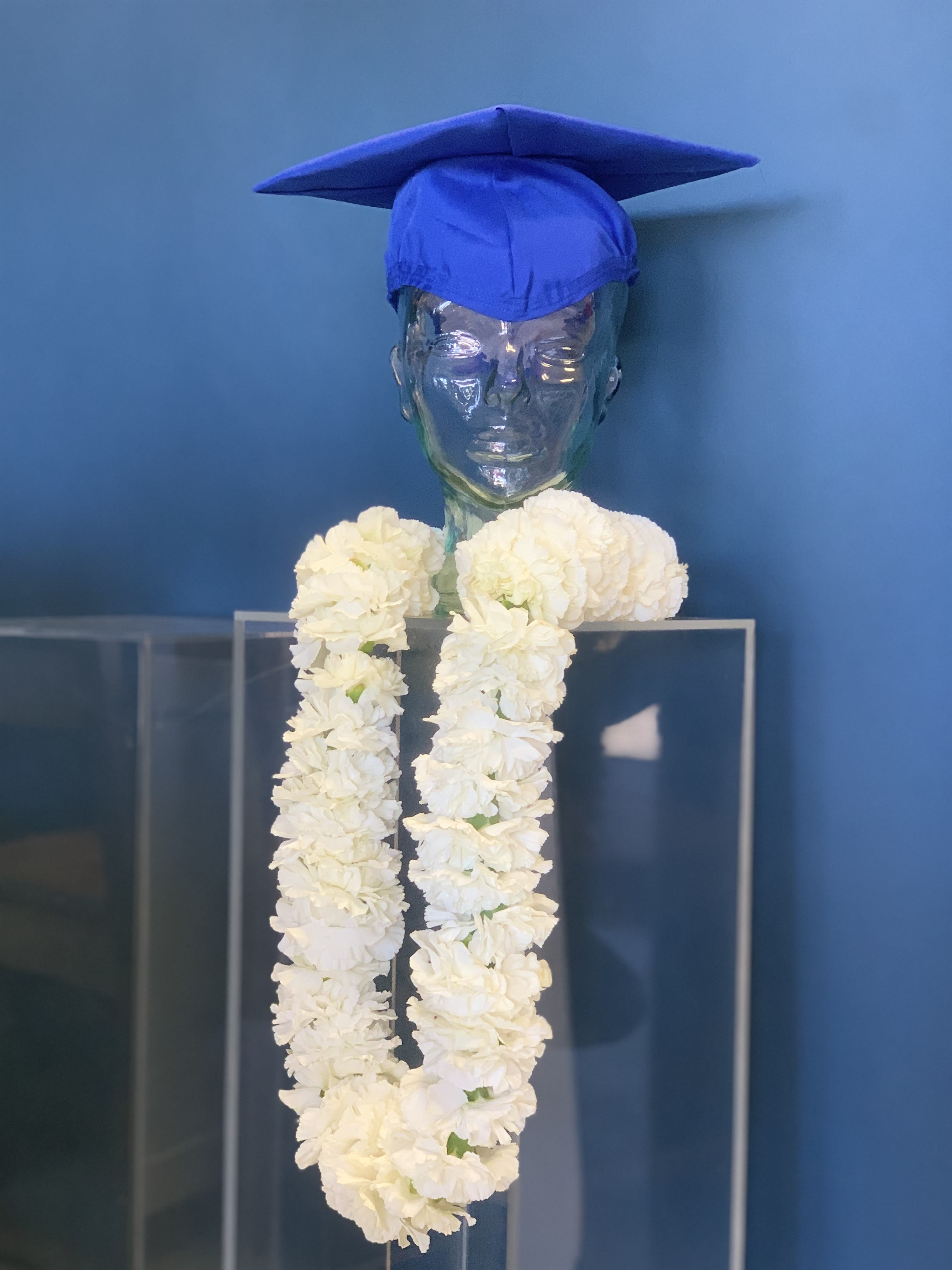White flower garland on a clear mannequin bust with a blue graduation cap
