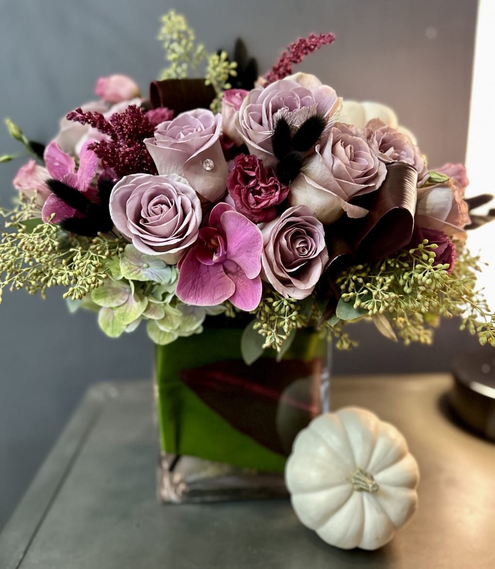 Pink and lavender rose bouquet in a green glass vase with a white pumpkin