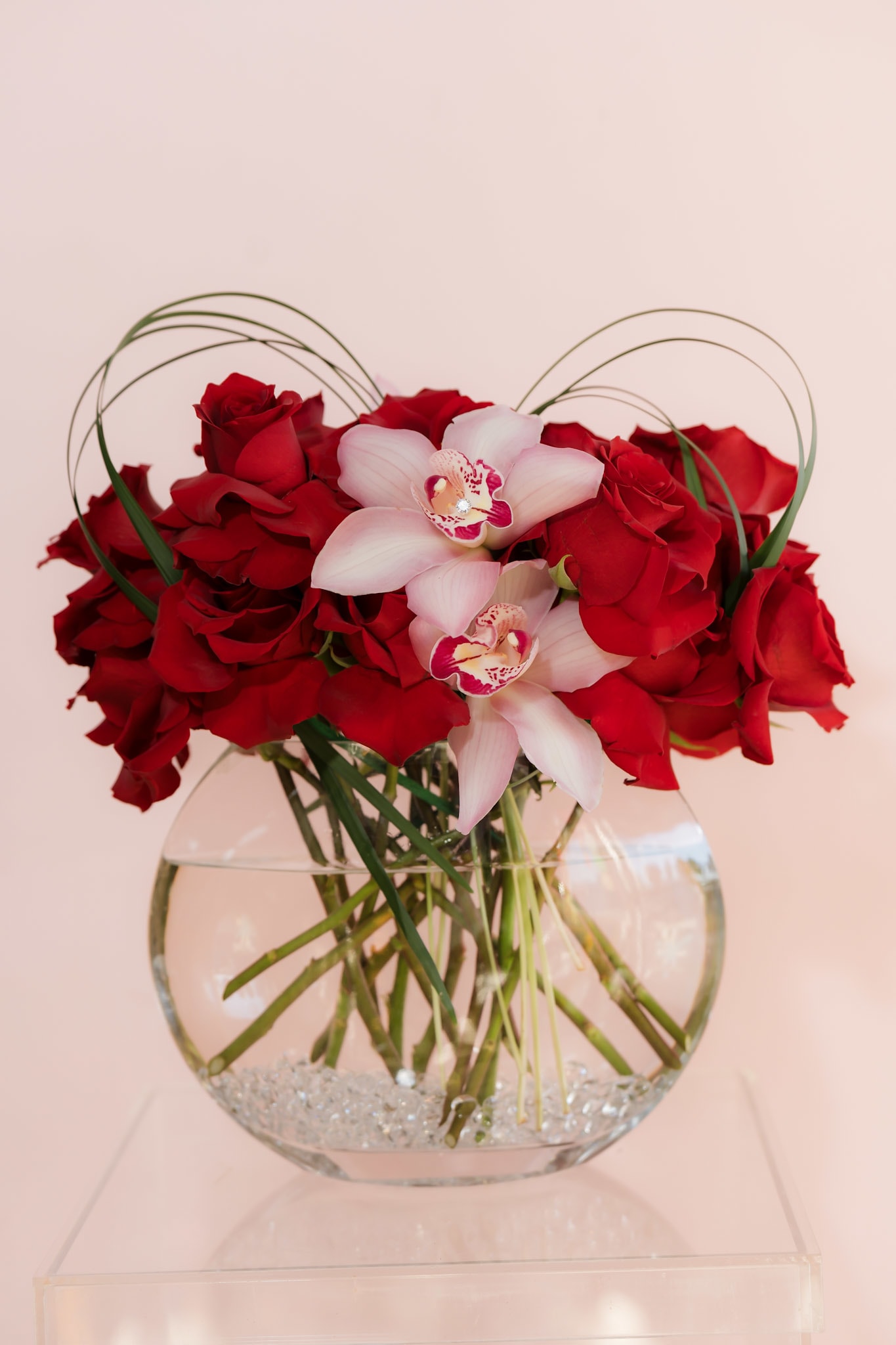 Red roses and pale pink orchids in a clear glass vase