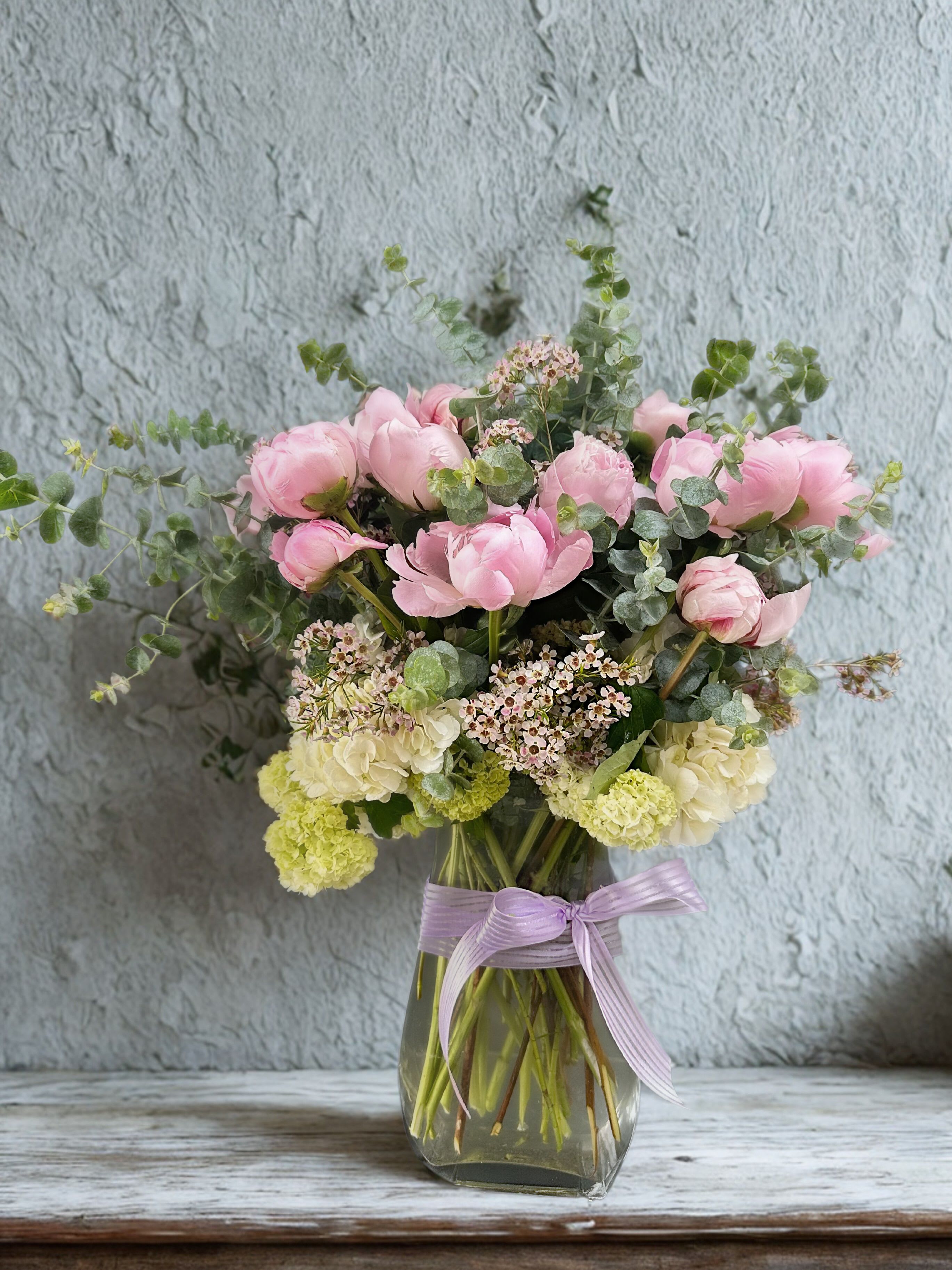 Pink and cream flowers in a glass vase with a lavender ribbon
