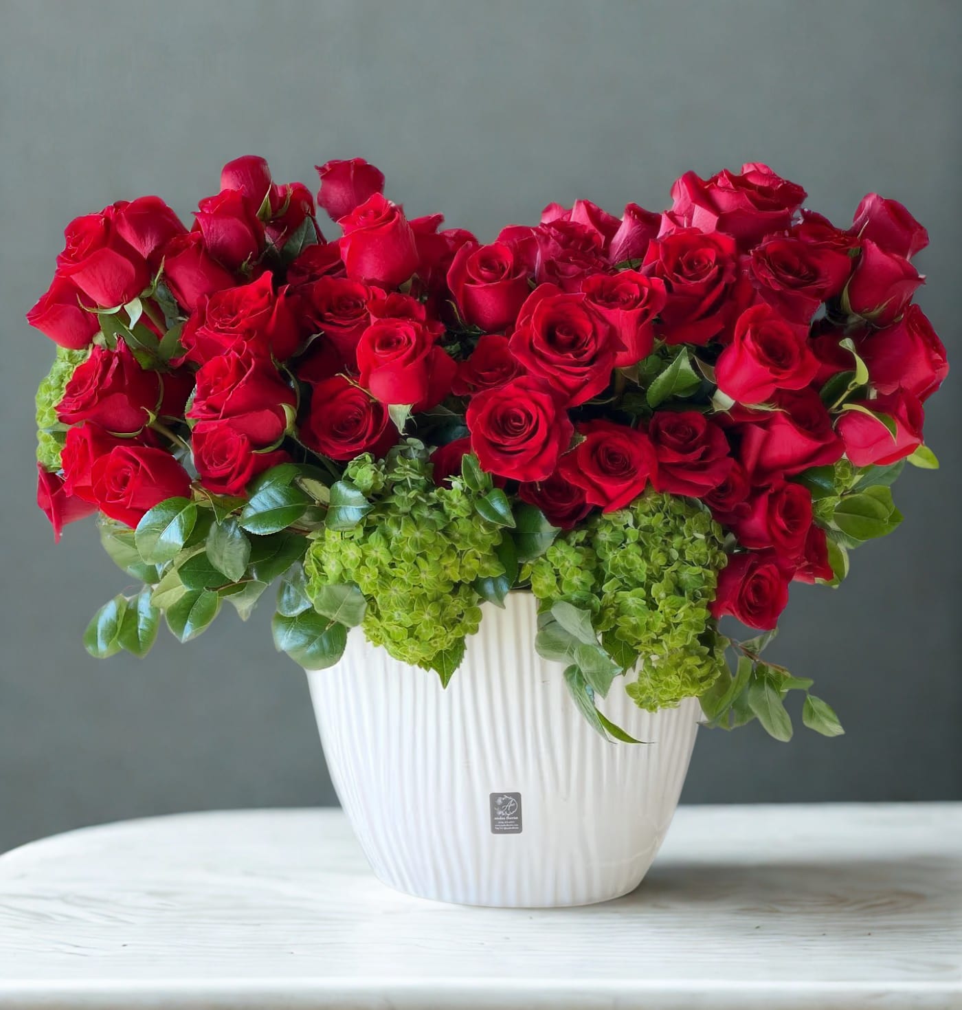 Red roses arranged in a white vase with green hydrangeas