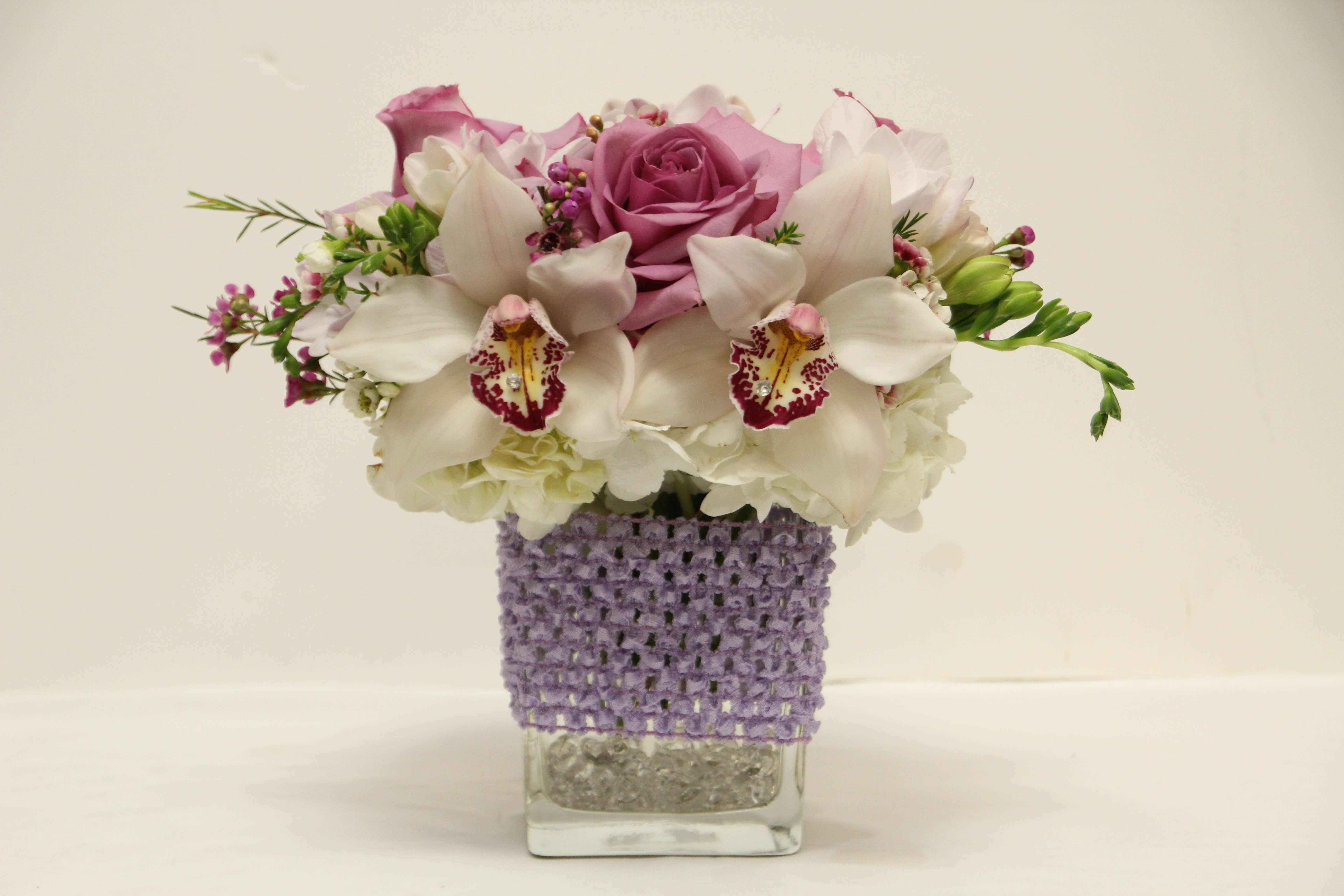 Pink roses and white orchids in a clear square vase with a purple wrap
