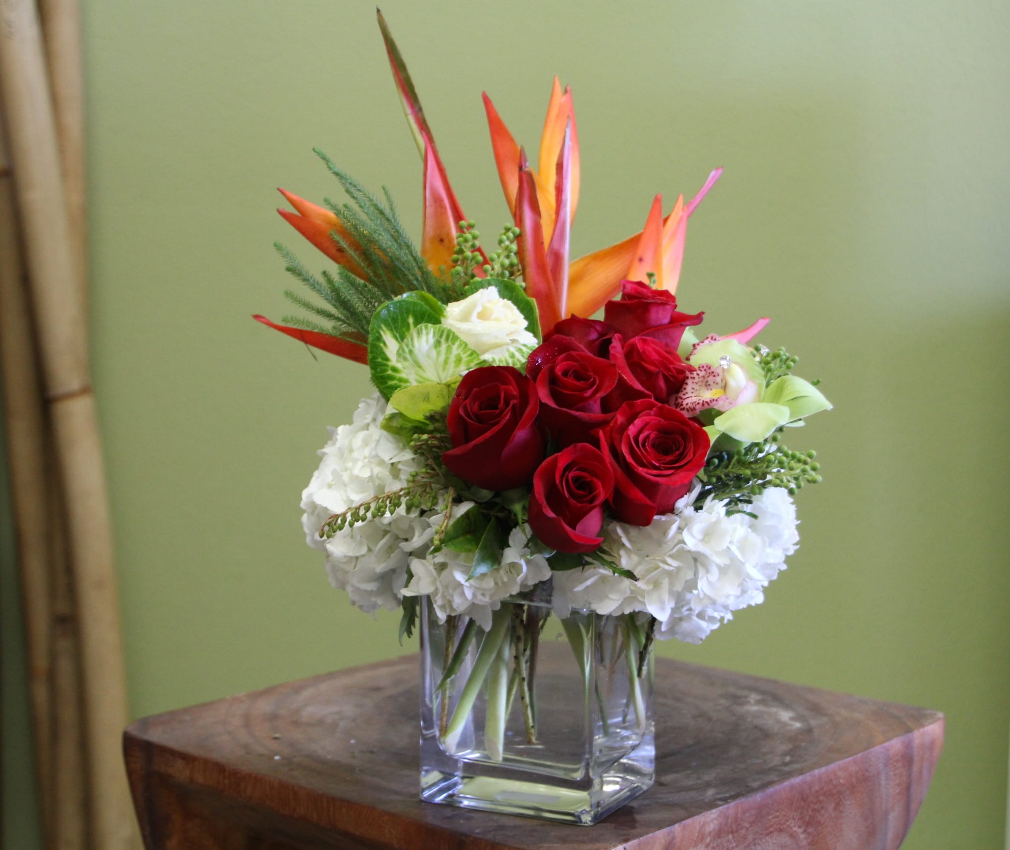 Red roses and white hydrangeas in a clear glass vase with orange tropical blooms
