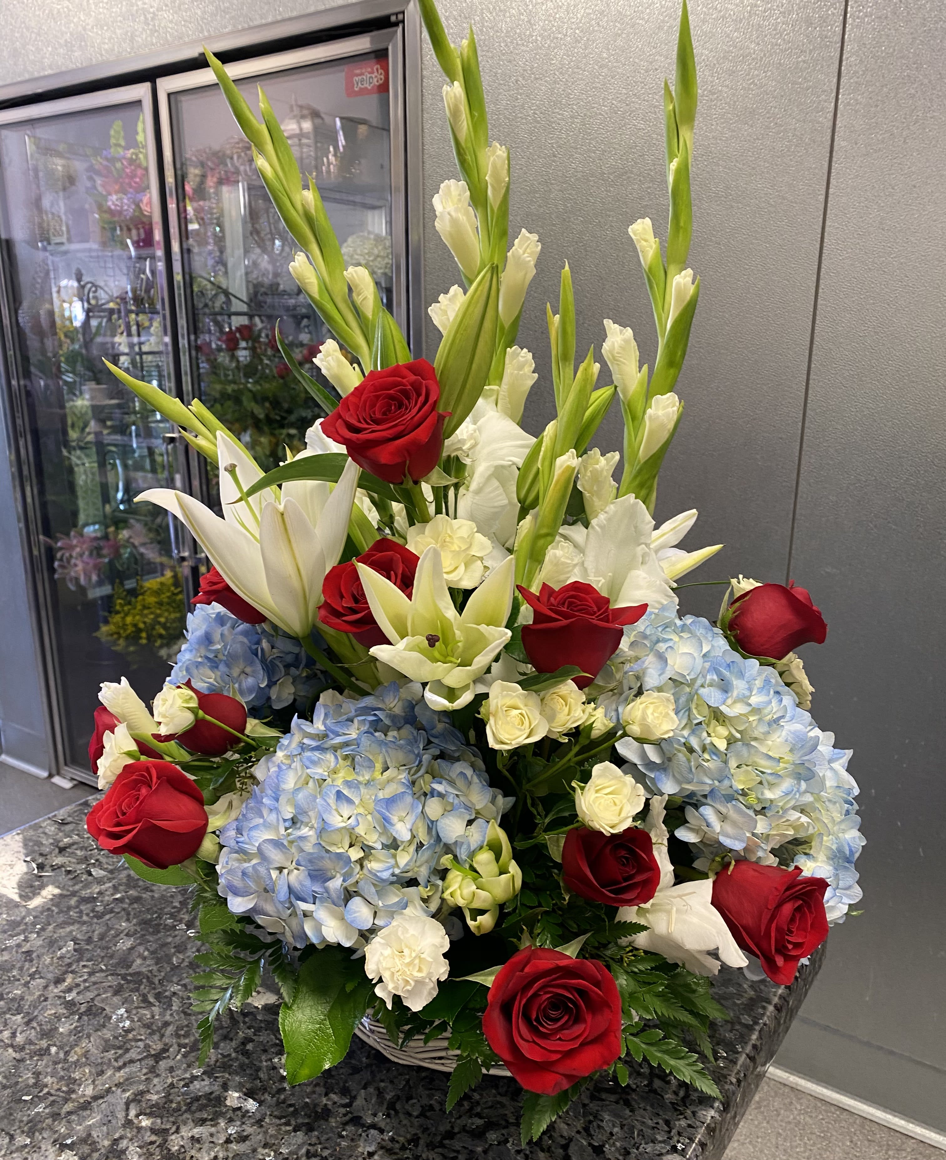 Red roses, white lilies, and blue hydrangeas in a basket arrangement