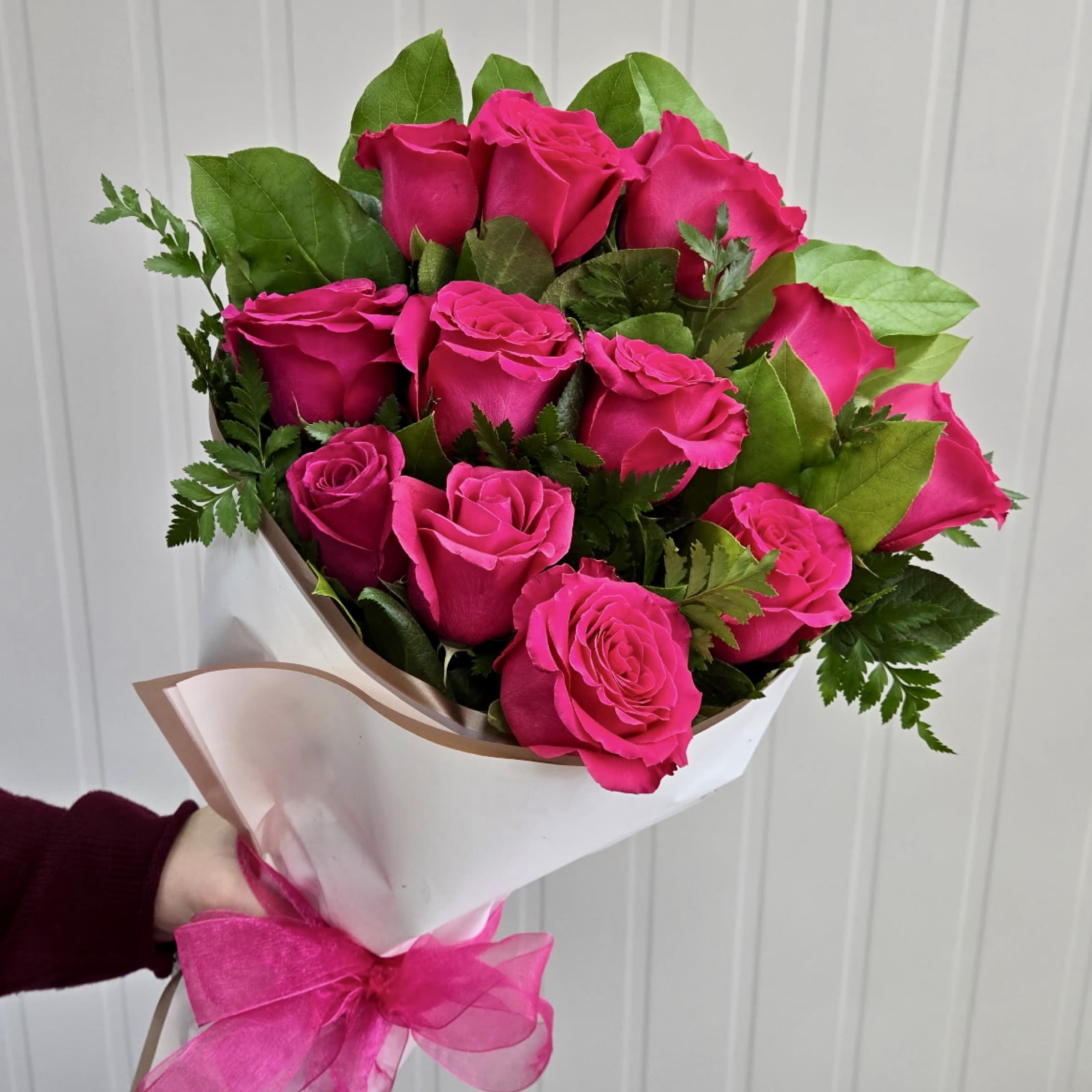 Bouquet of bright pink roses wrapped in white paper with a pink ribbon