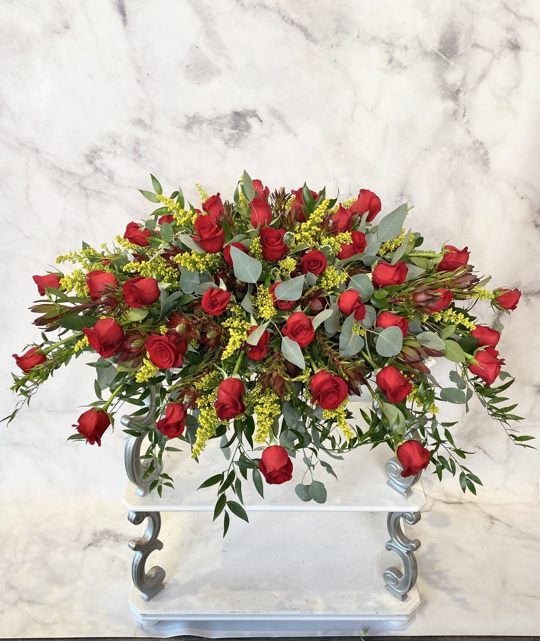 Large arrangement of red roses with yellow filler flowers on a white stand