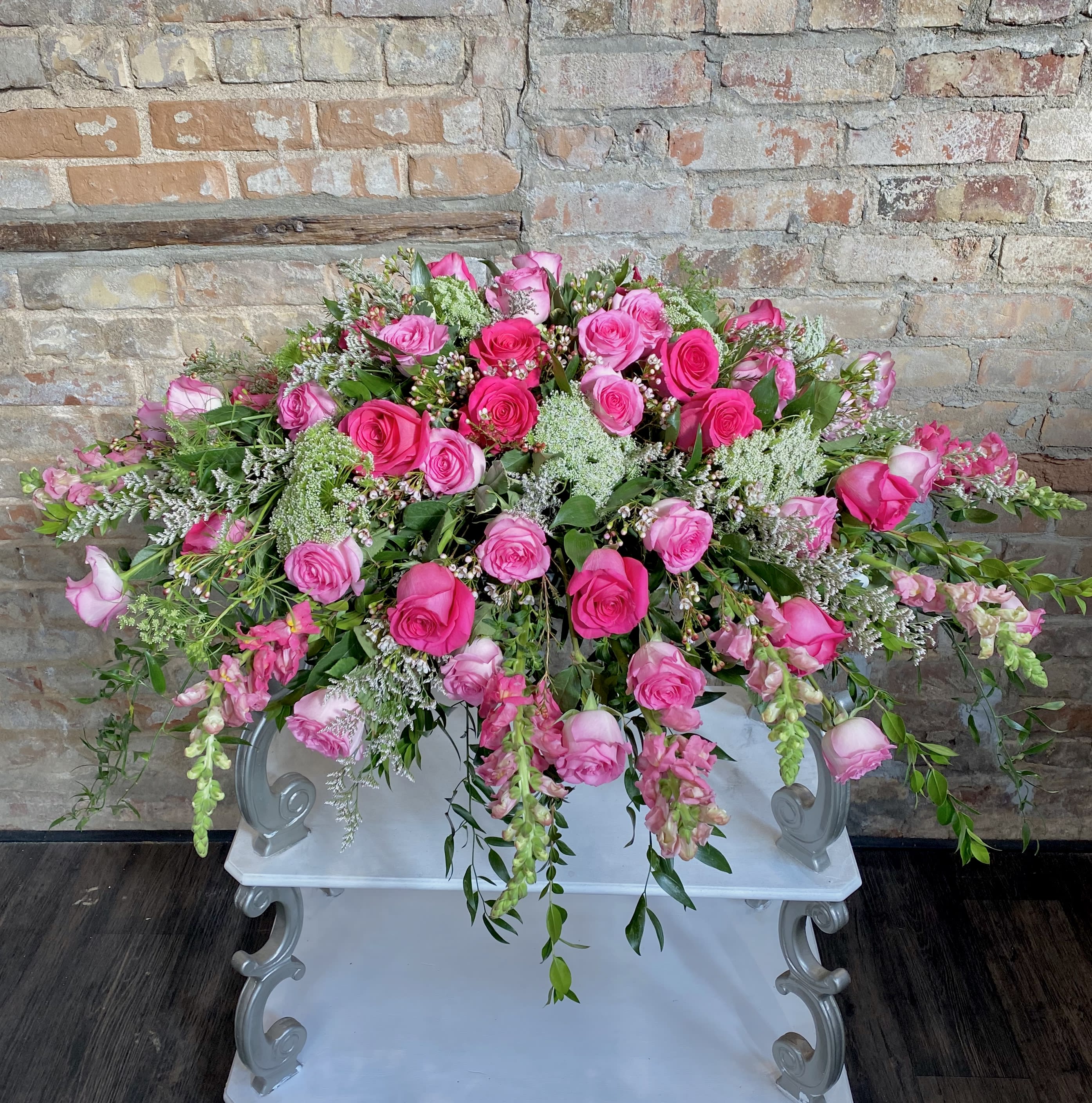 Large pink rose arrangement with trailing greenery on a white pedestal