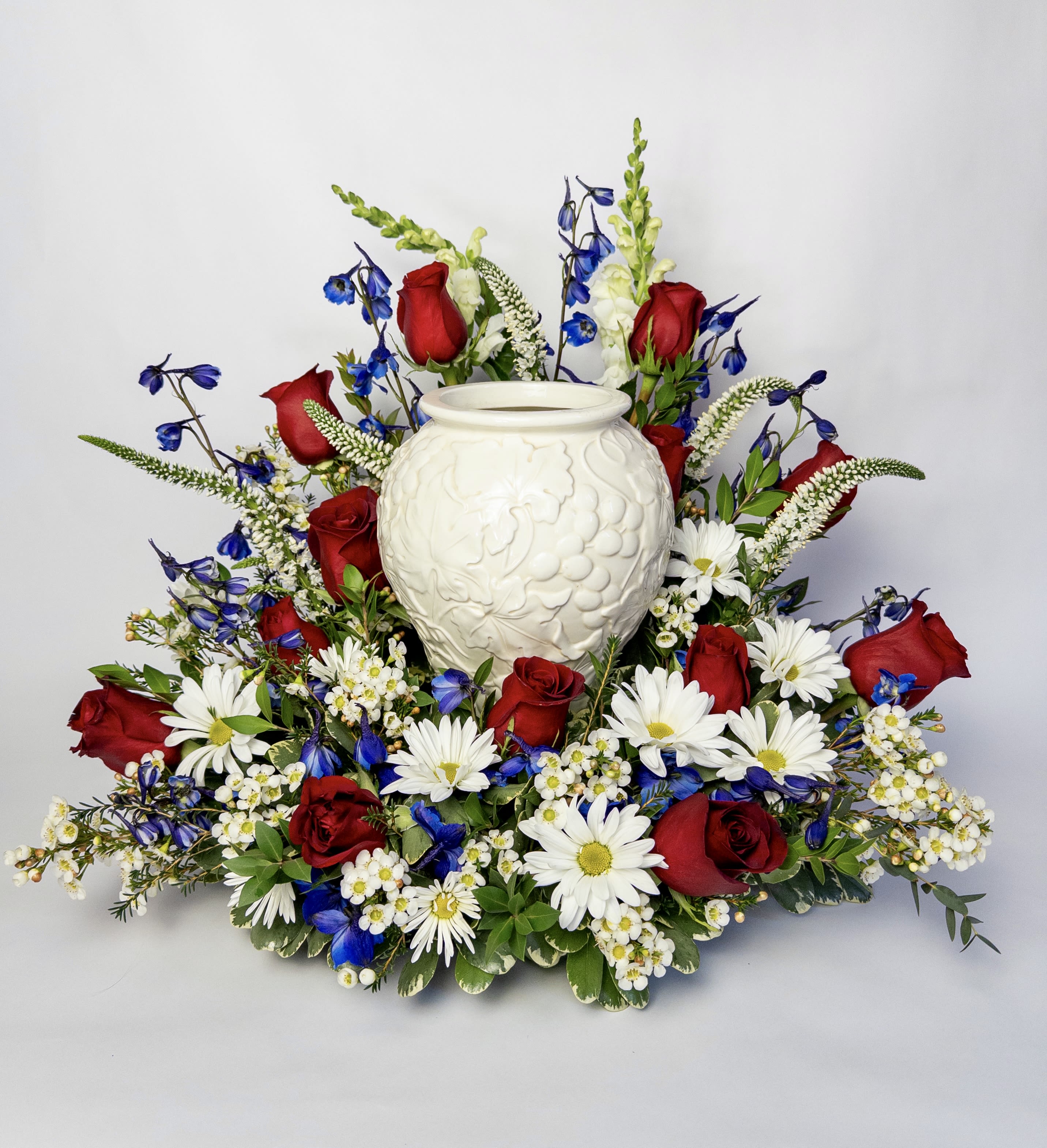 Red roses and white daisies arranged around a white urn vase
