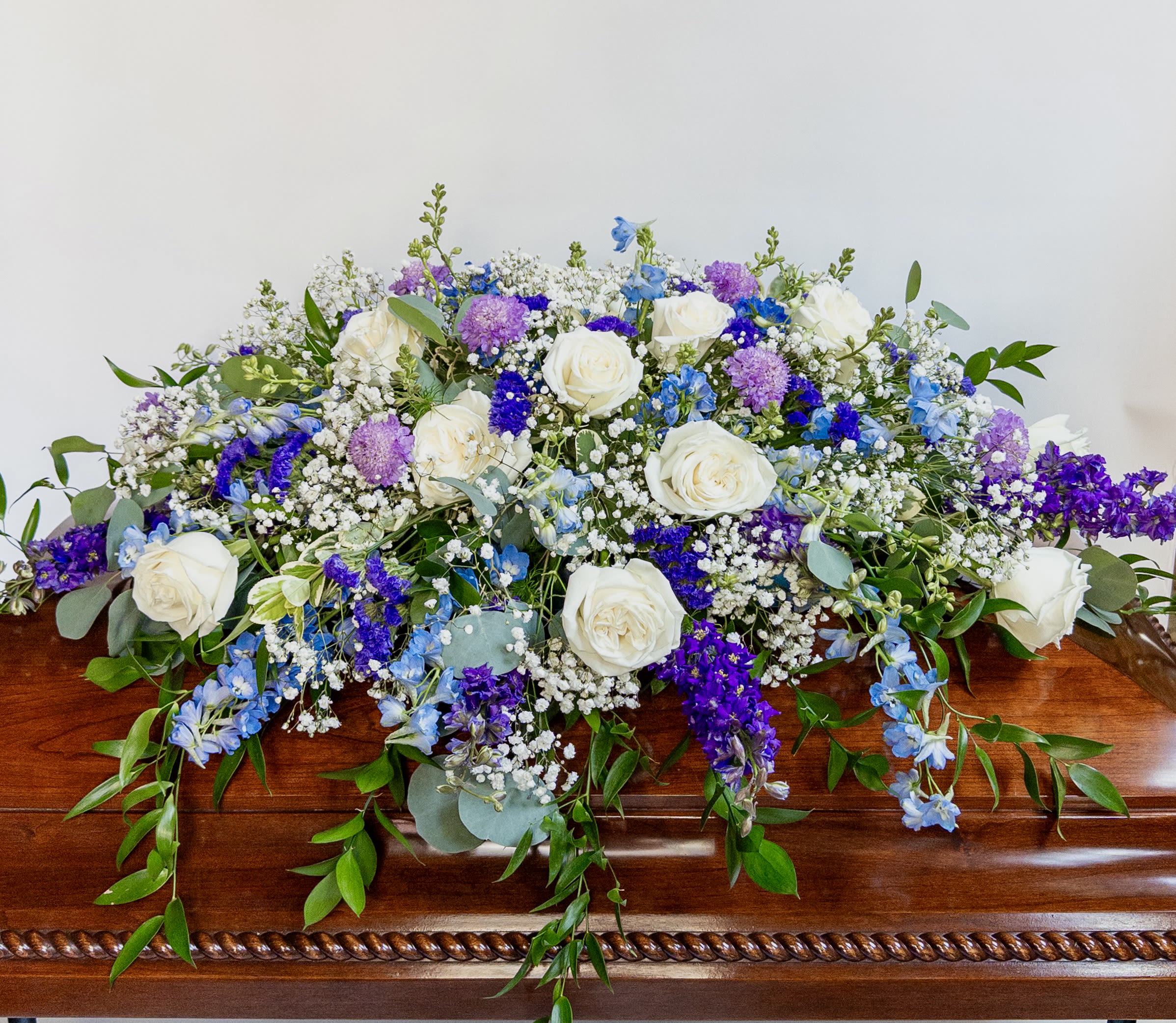 White roses and purple-blue flowers arranged on a wooden casket
