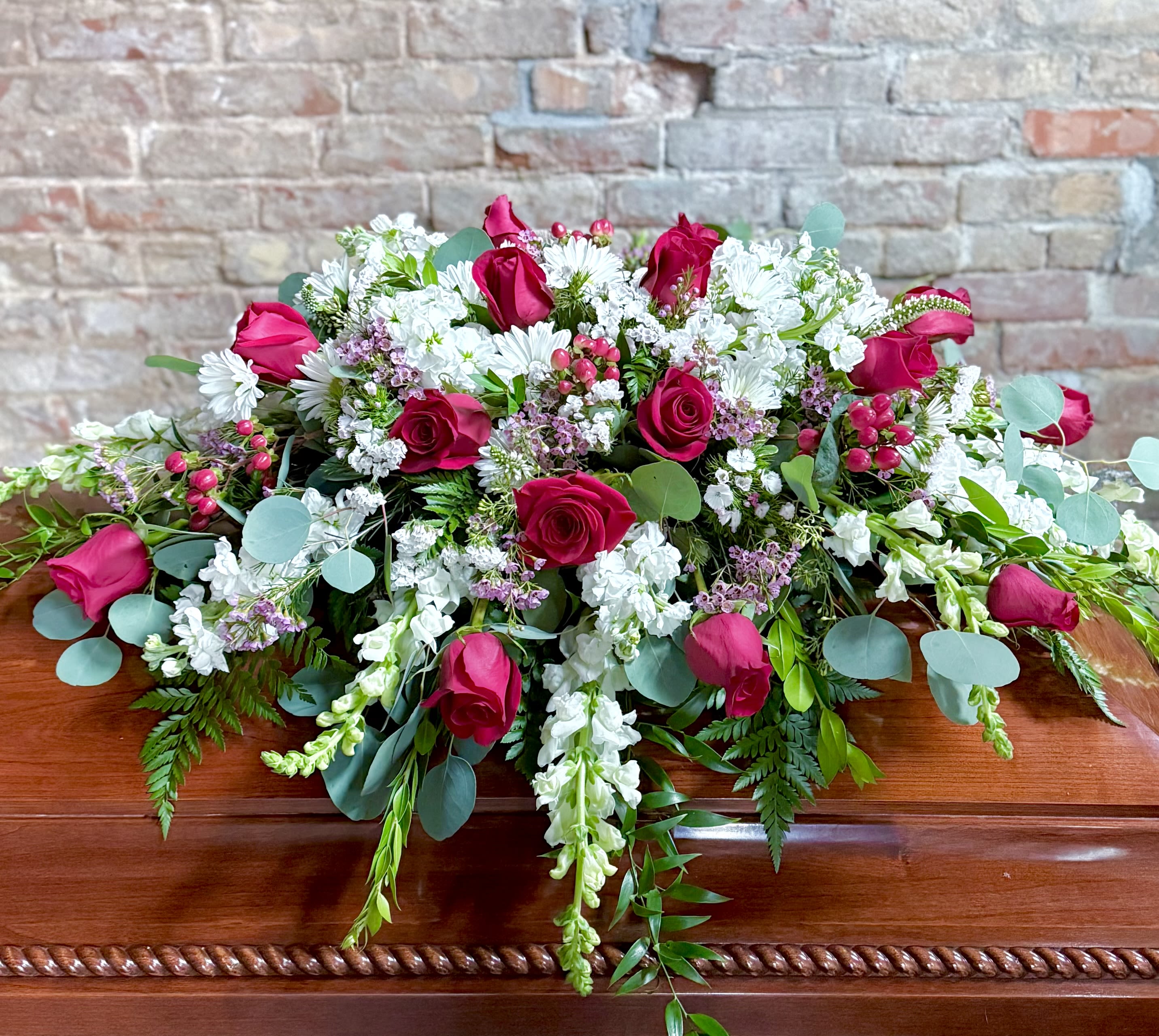 Casket spray with pink roses, white flowers, and greenery