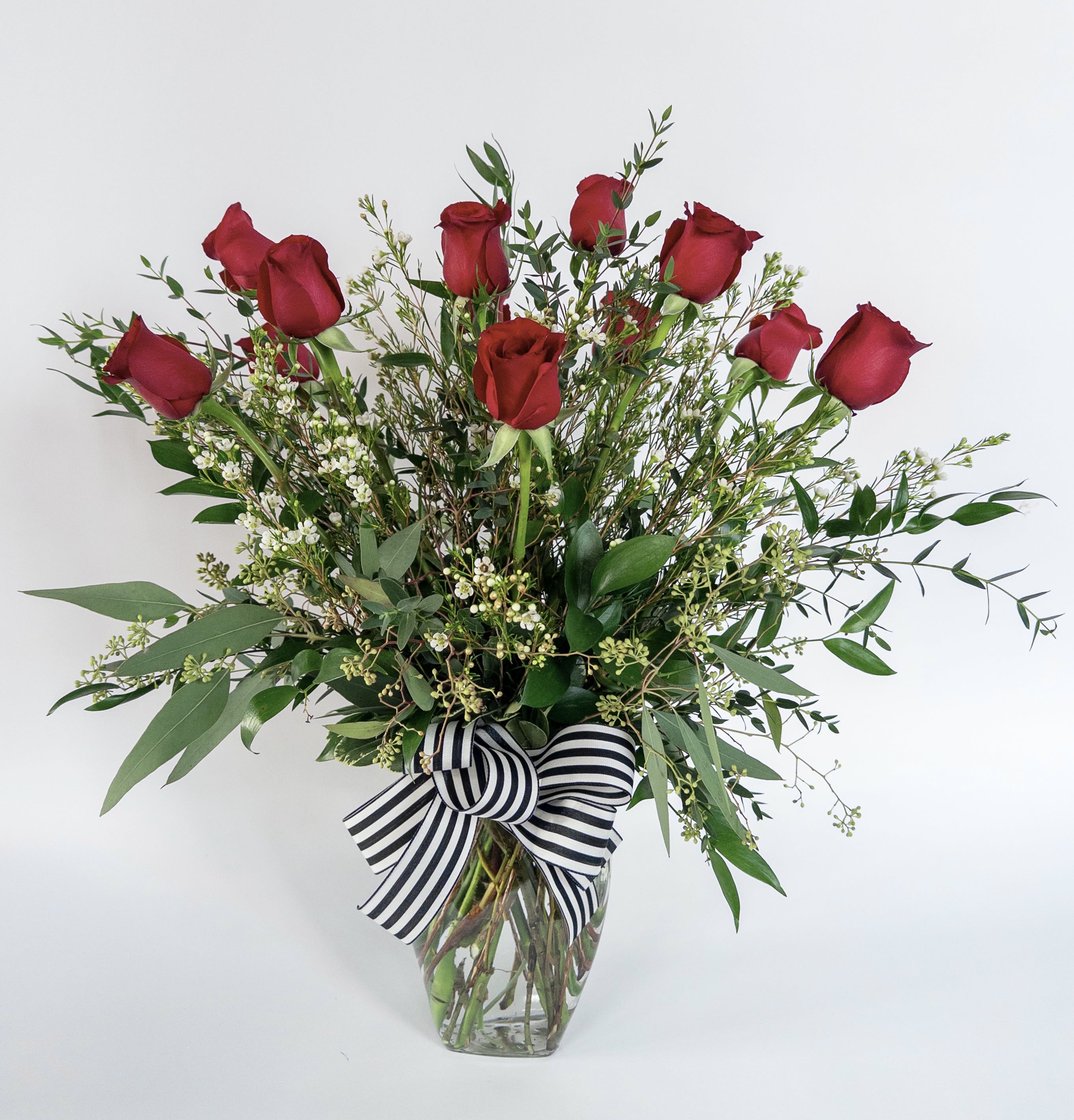 Red roses in a clear glass vase with a black-and-white striped bow