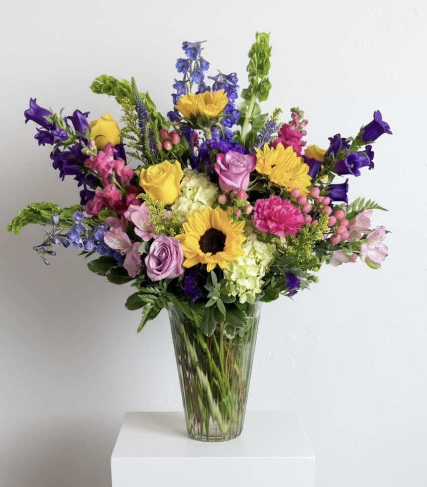 Seasonal Bright Mix- size large  - All the bright colors in a tall clear vase. Filled with a mix of delphinium, sunflowers, hydrangeas, Veronica, companula and tulips to name a few. 