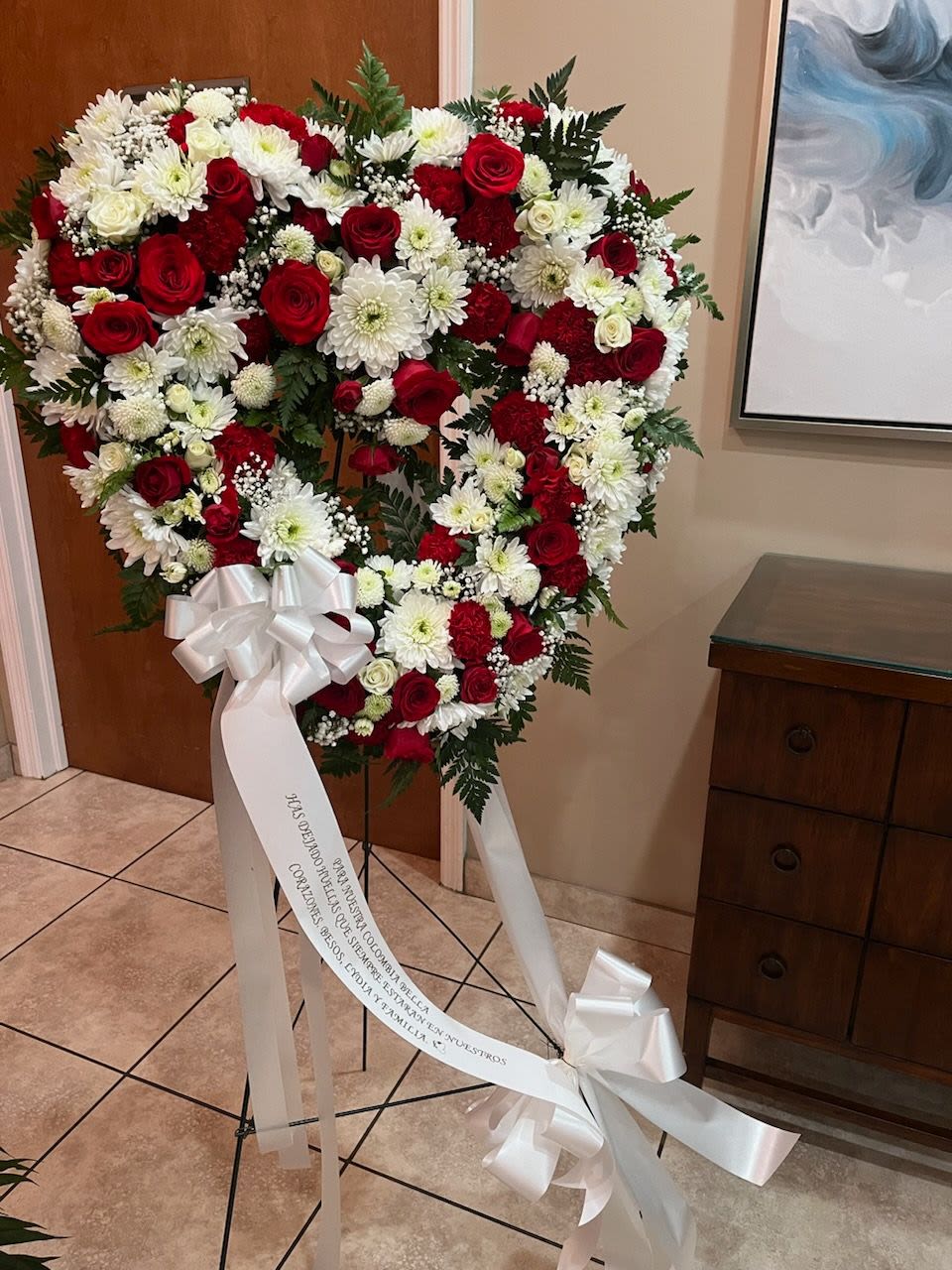 Heart-shaped standing wreath of red and white flowers with a white ribbon