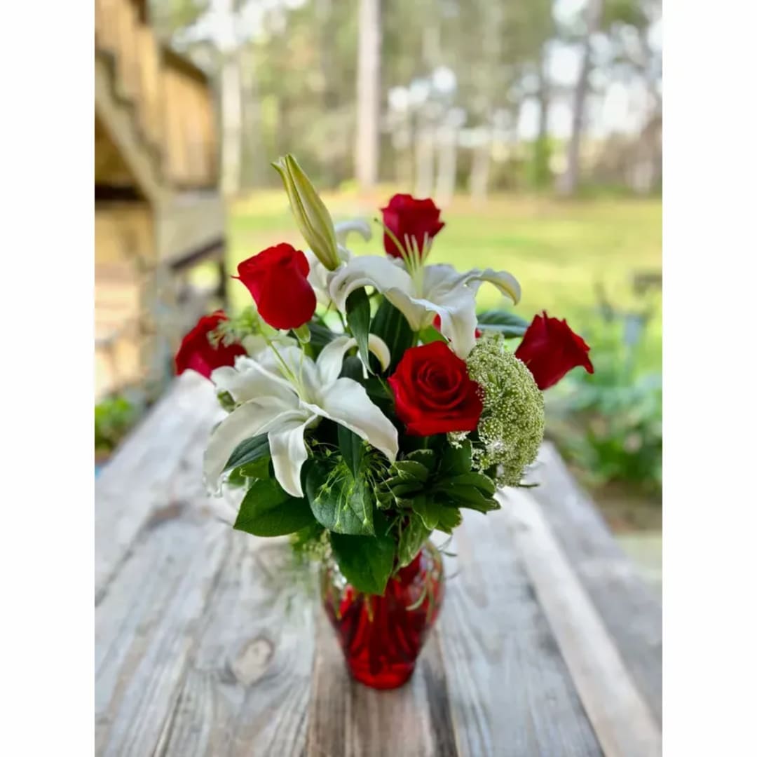 Red roses and white lilies in a red glass vase on a wooden table