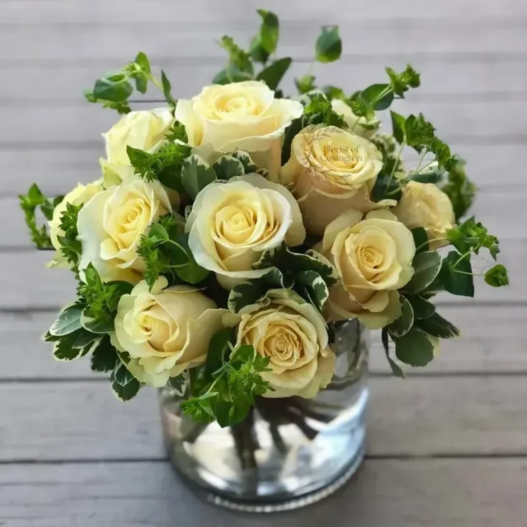 Cream roses arranged in a clear glass vase with green foliage
