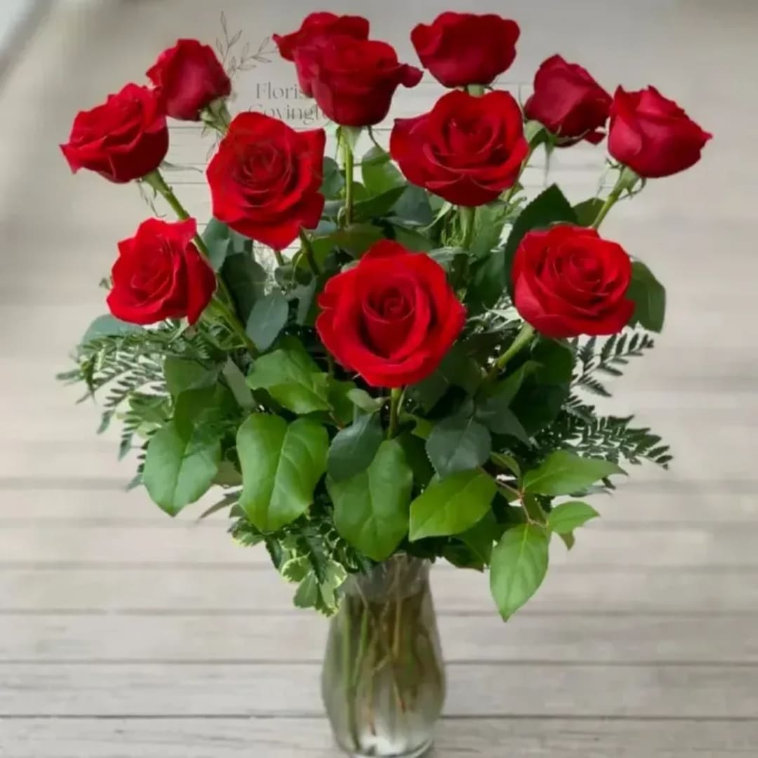 Red roses arranged in a clear glass vase with mixed greenery