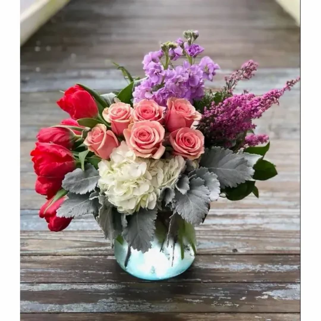 Mixed bouquet of pink roses, red tulips, and purple flowers in a glass vase