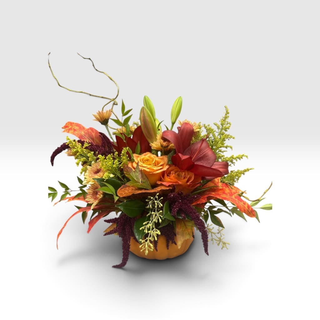 Autumn floral arrangement in a pumpkin-shaped container with orange and red blooms