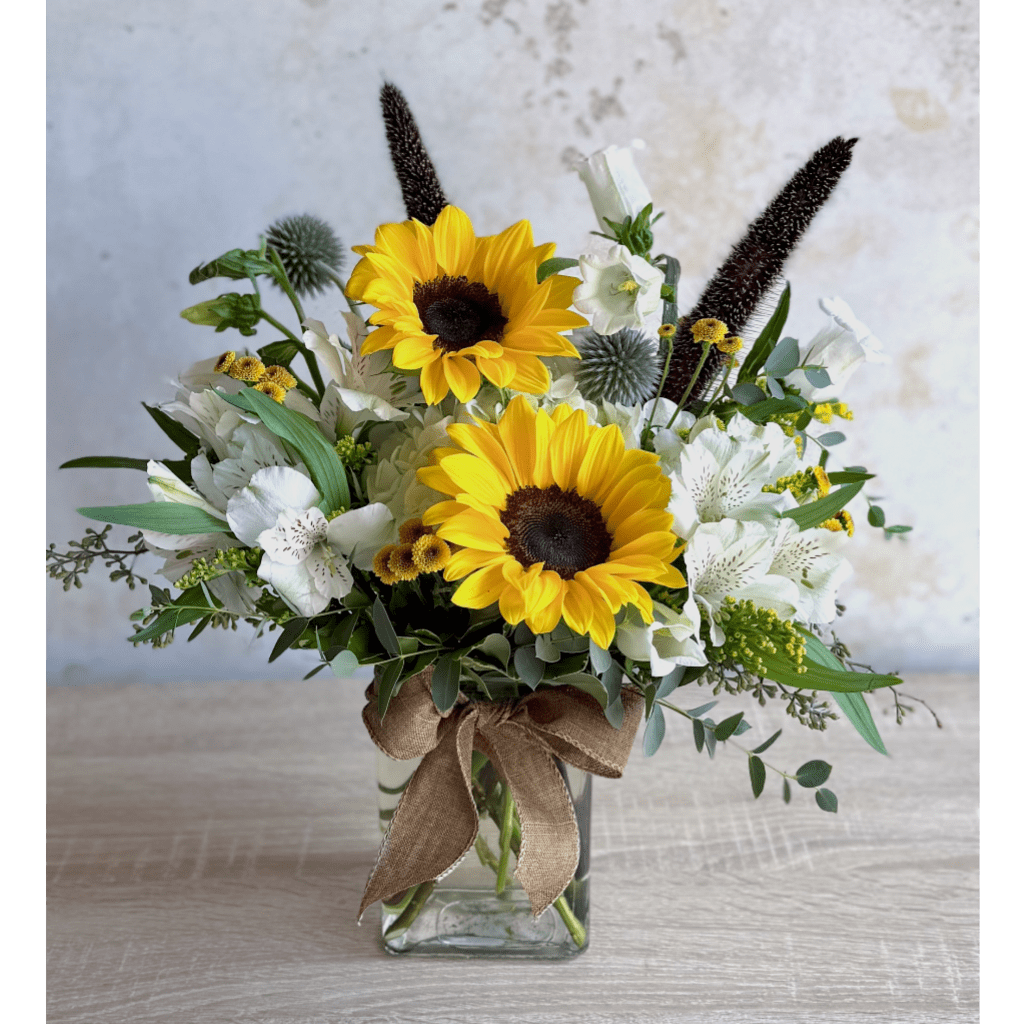 Sunflower arrangement in a clear glass vase with white flowers and a burlap bow